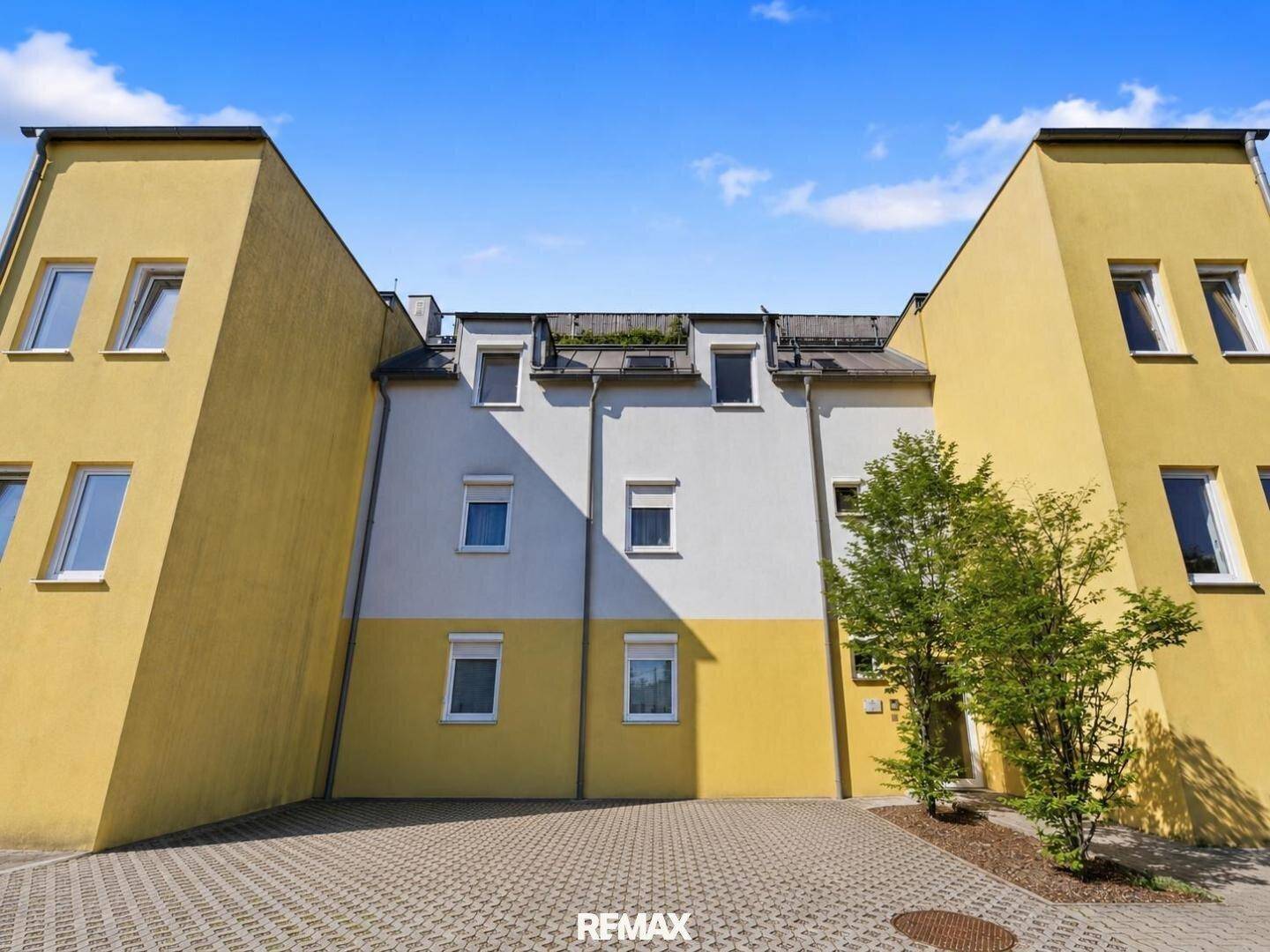 Moderne Wohnanlage mit gelb-weißer Fassade und großen Fenstern unter blauem Himmel.