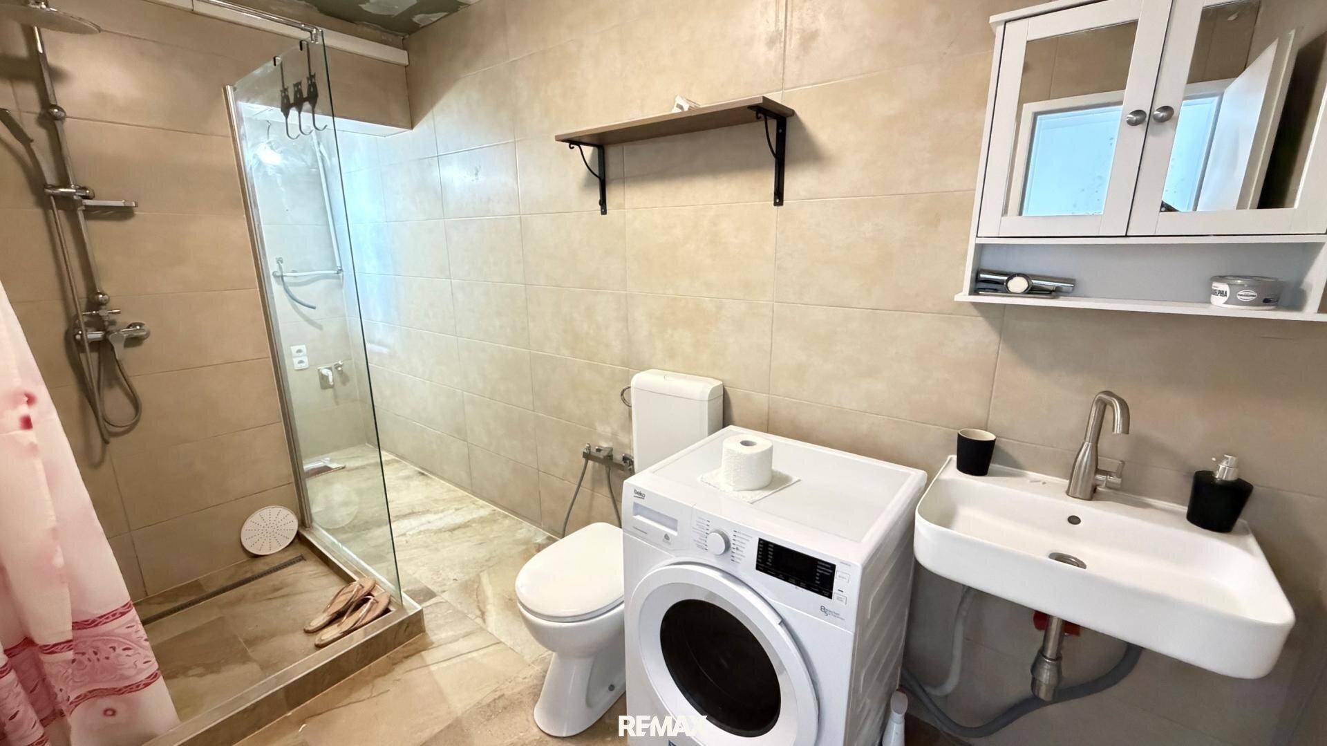 Funktionales Badezimmer mit Dusche, Waschbecken, Toilette und Waschmaschine.