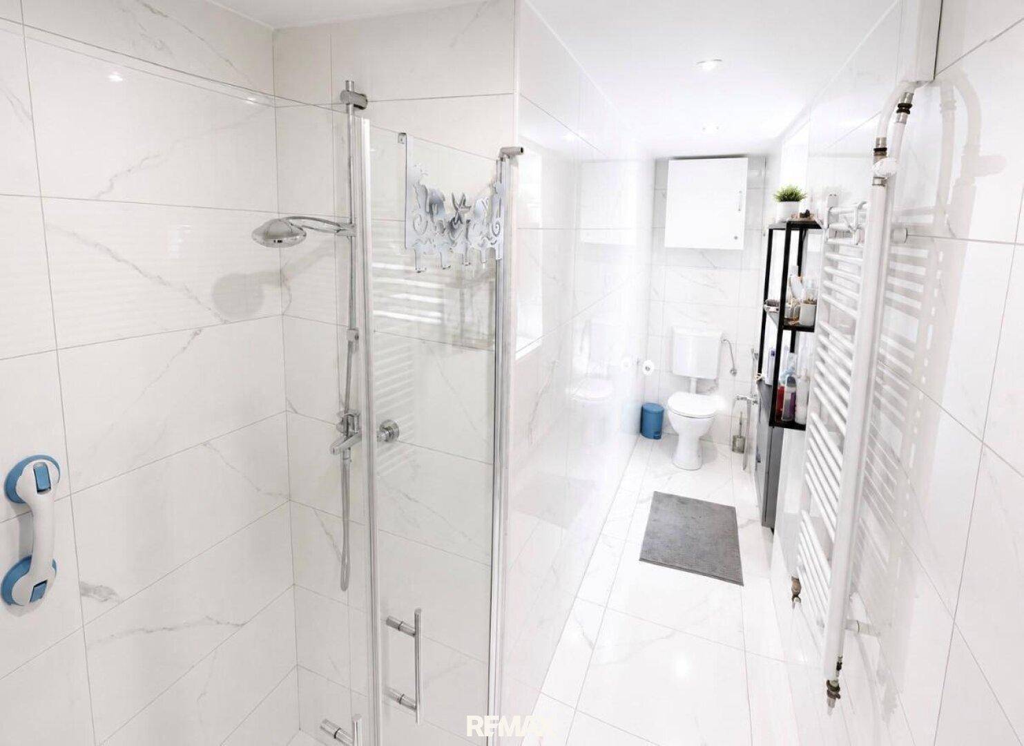 Modernes Badezimmer mit weißen Marmorfliesen, ebenerdiger Dusche und Handtuchheizkörper.