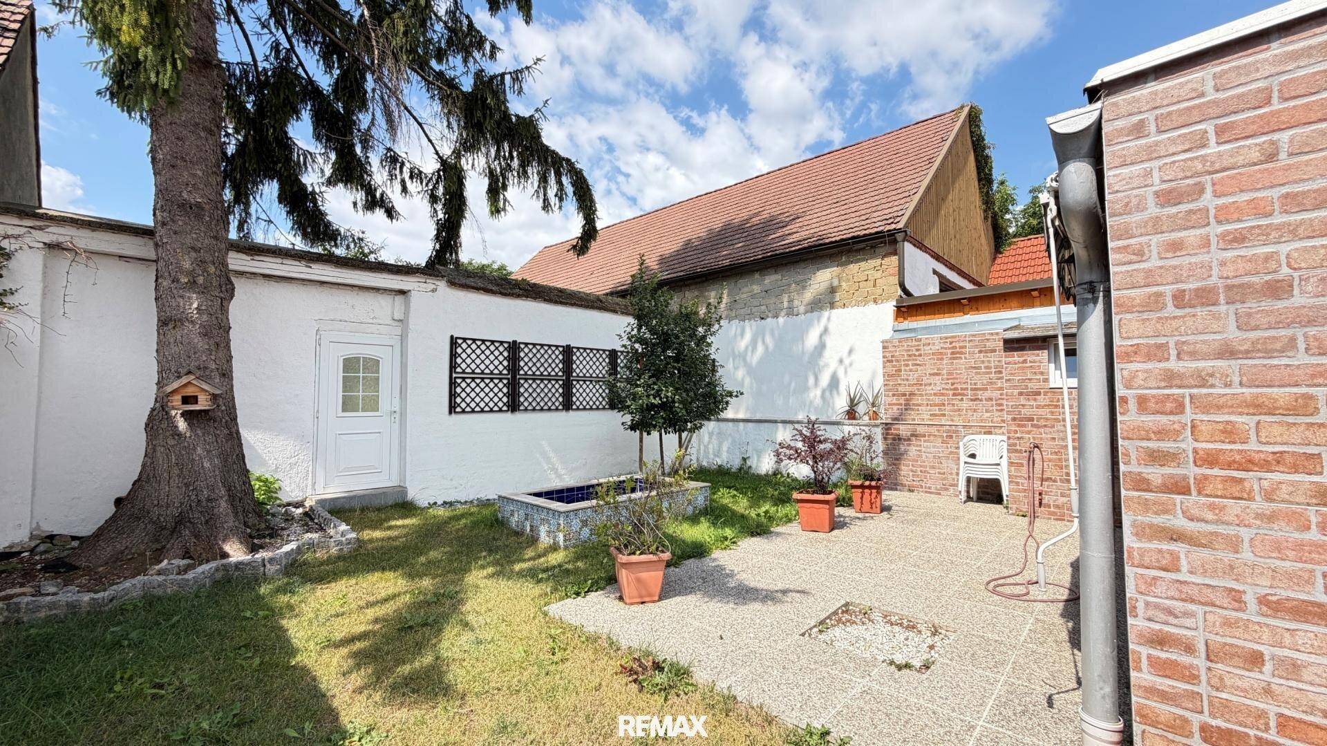Kleiner Gartenbereich mit Rasen, Bäumen und einem gepflasterten Sitzbereich.