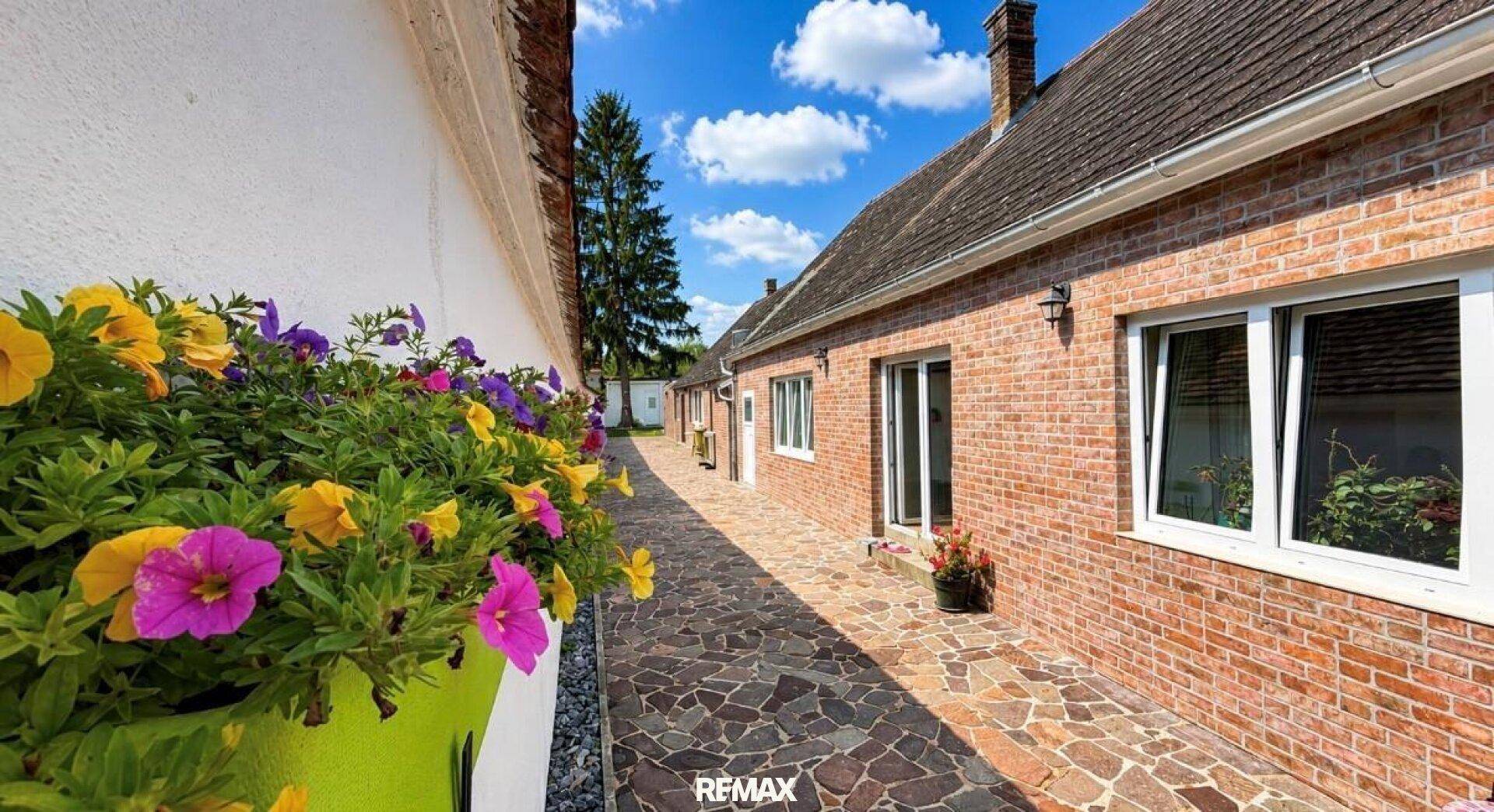 Außenbereich des Hauses mit Ziegelmauerwerk und gepflastertem Weg unter blauem Himmel.