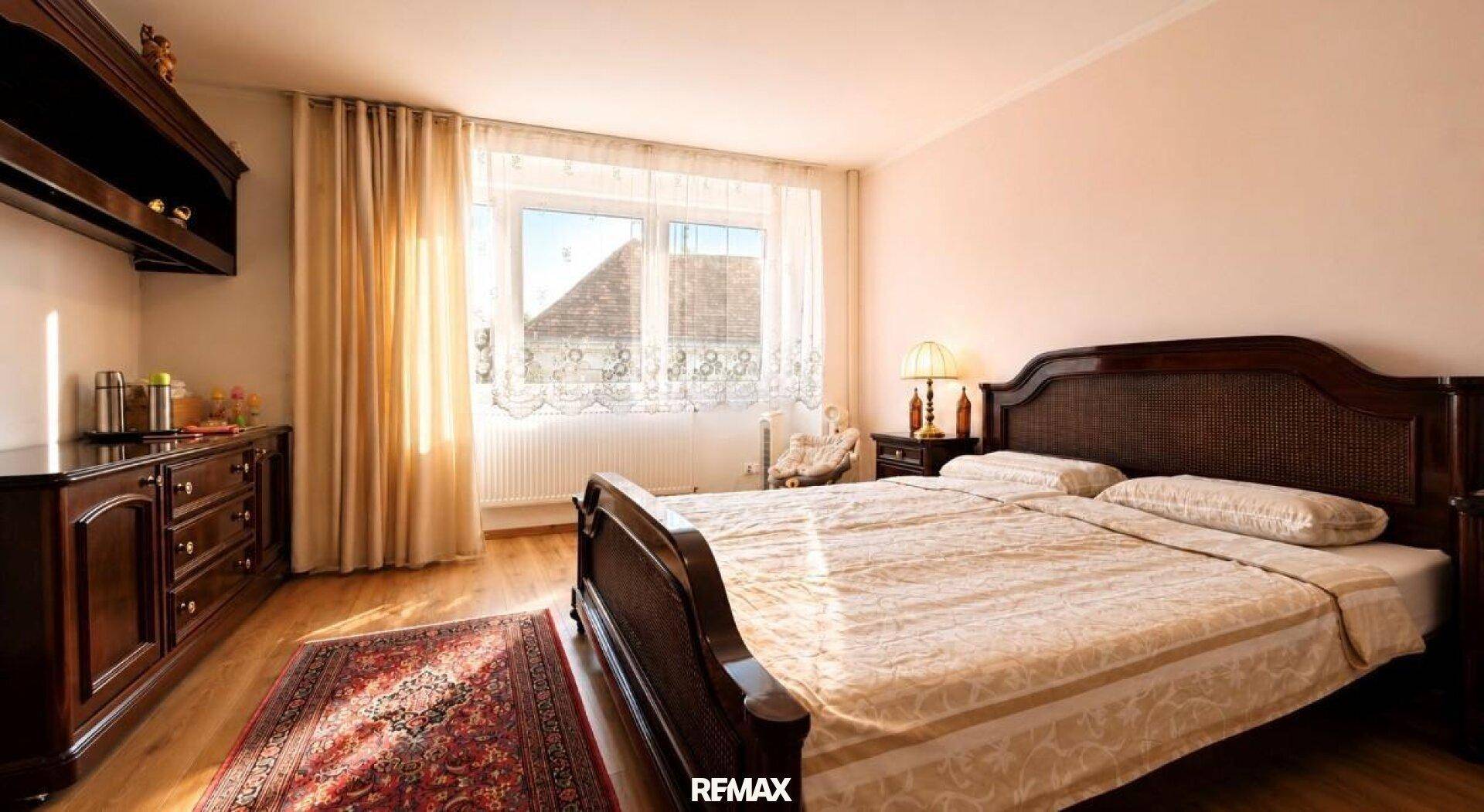 Gemütliches Schlafzimmer mit Doppelbett, Holzmöbeln und Vorhängen vor dem Fenster.