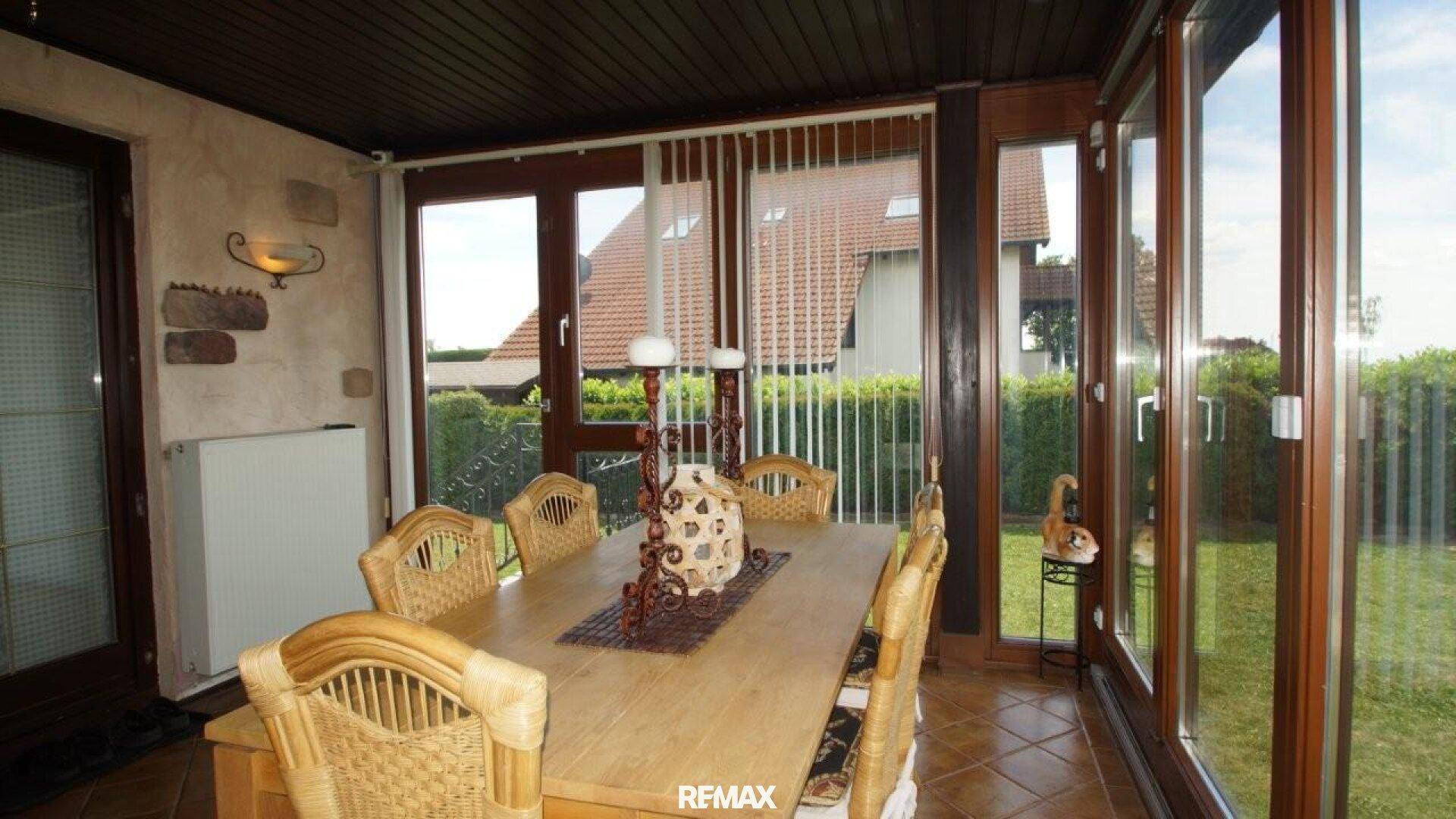 Heller Wintergarten mit Essbereich, Korbstühlen und Blick ins Grüne.