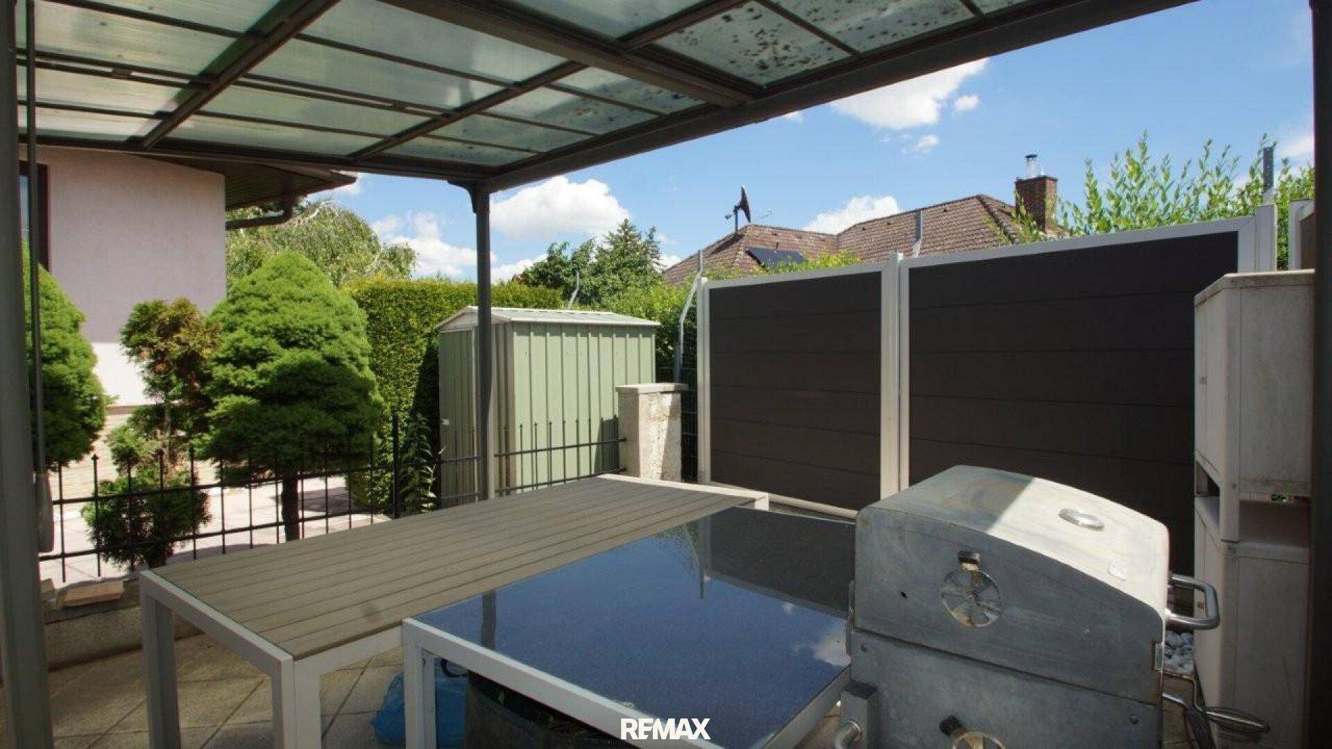 Überdachte Terrasse mit Esstisch, Grill und Blick auf den Garten.
