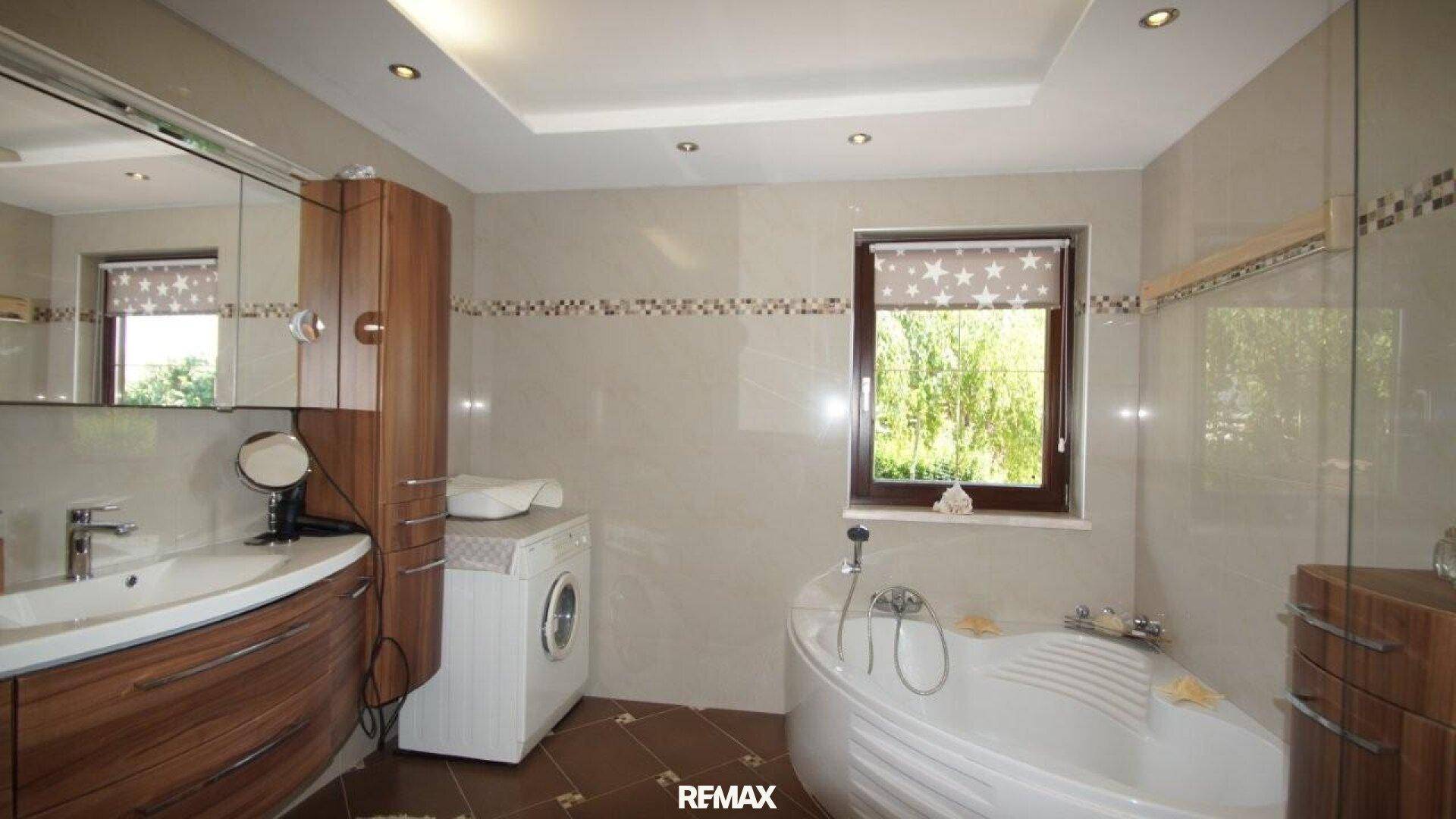 Modernes Badezimmer mit Eckbadewanne, Waschmaschine und Fenster für Tageslicht.