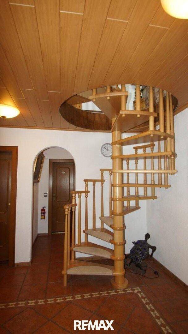Eingangsbereich mit hölzerner Wendeltreppe, Terrakotta-Fliesen und Holztüren.