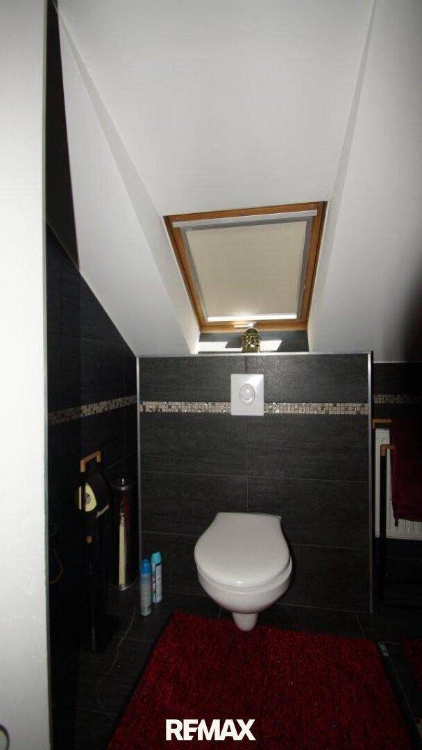 Modernes Gäste-WC im Dachgeschoss mit dunklen Fliesen, Wand-WC und Dachfenster.