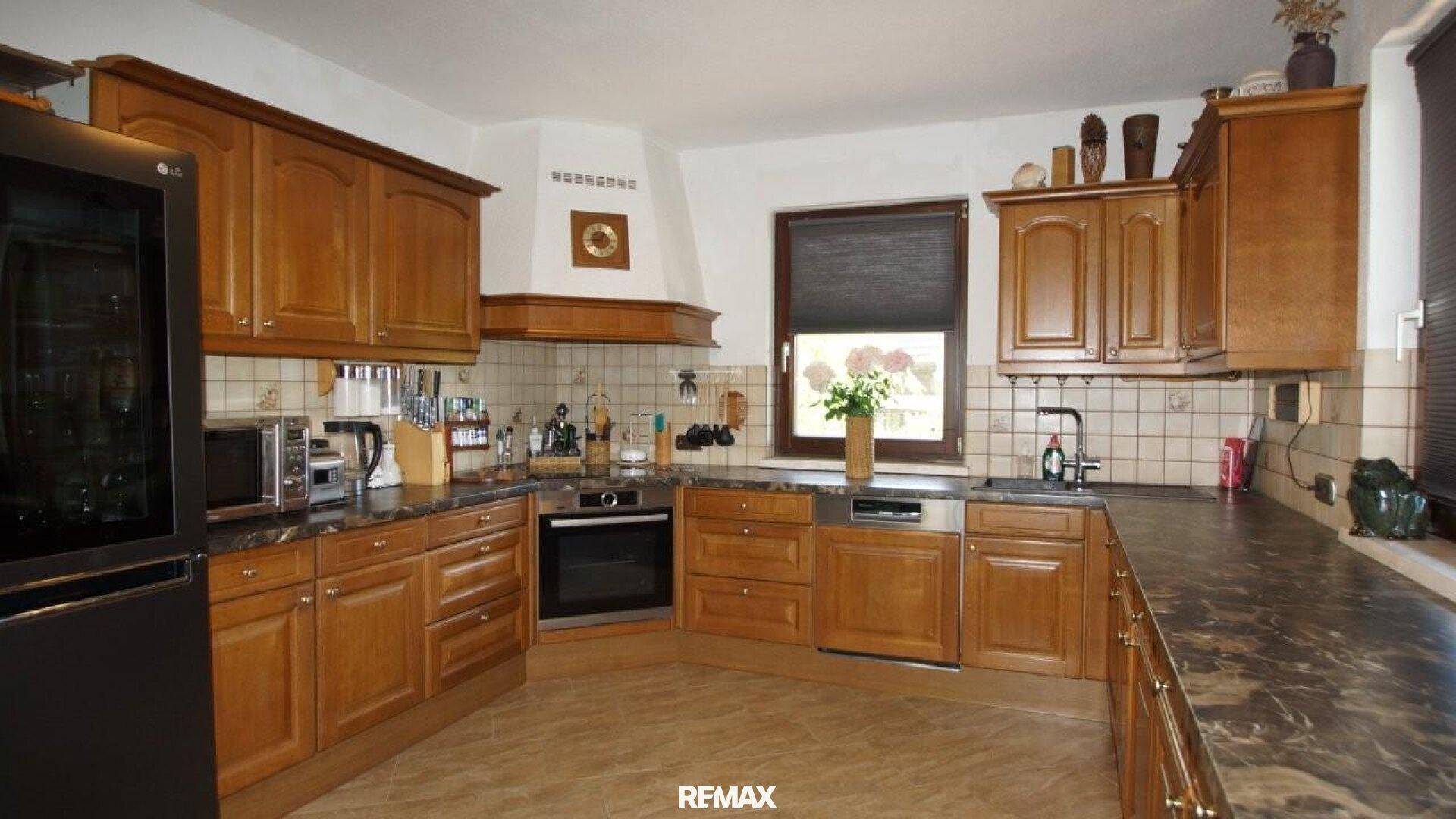 Voll ausgestattete Holzküche mit Kühlschrank, Backofen und dunkler Arbeitsplatte.
