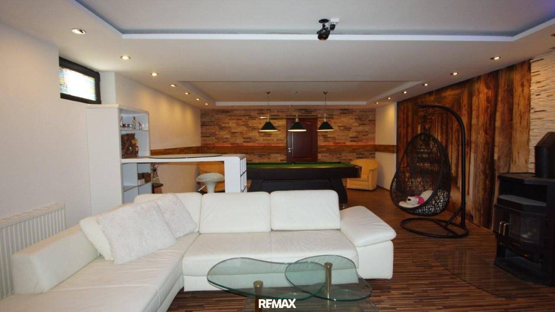 Geräumiger Hobbyraum im Keller mit Billardtisch, weißem Sofa und Holzvertäfelung.