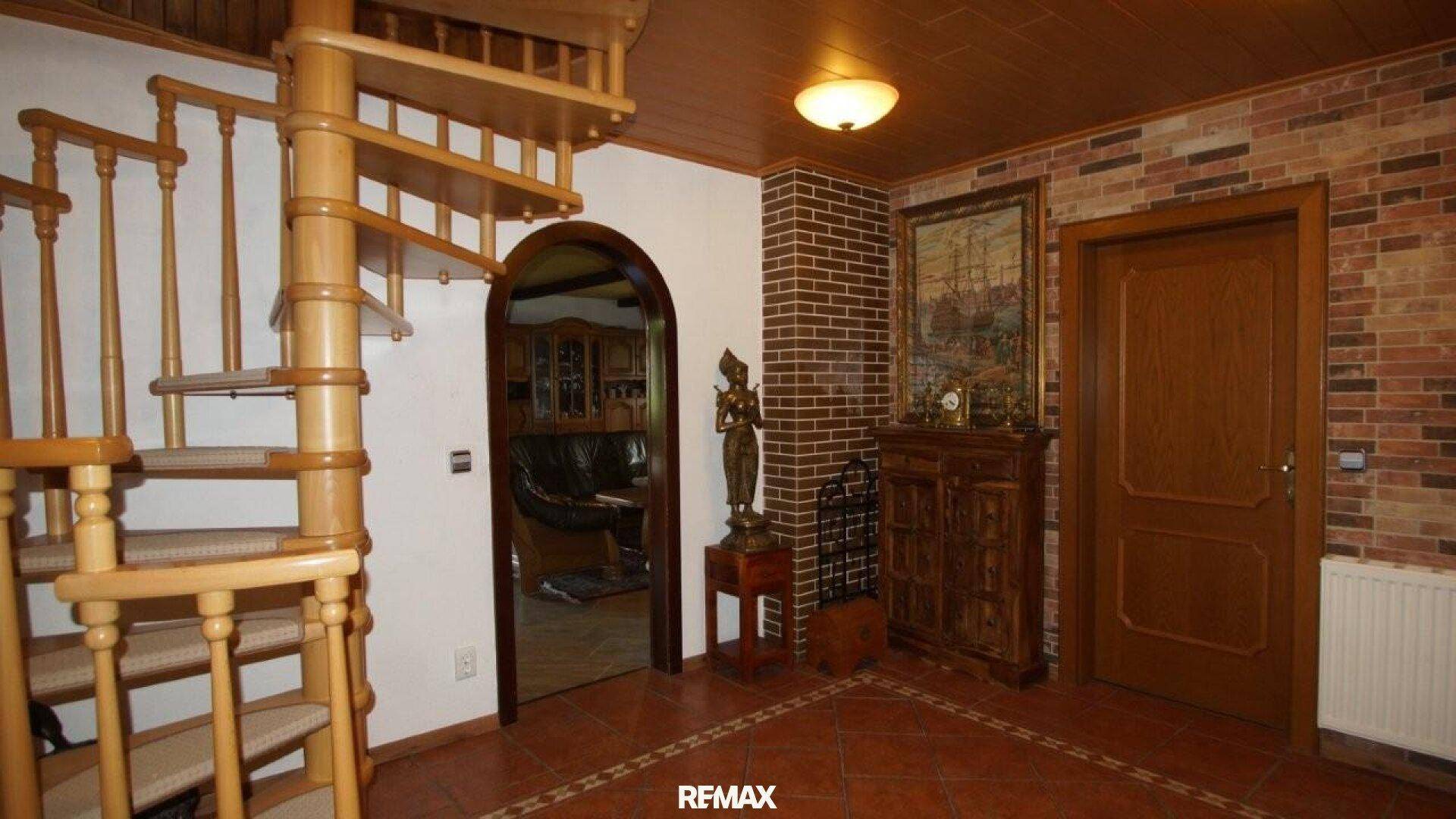 Eingangsbereich mit Wendeltreppe aus Holz, Ziegelwandakzenten und Terrakotta-Fliesenboden.