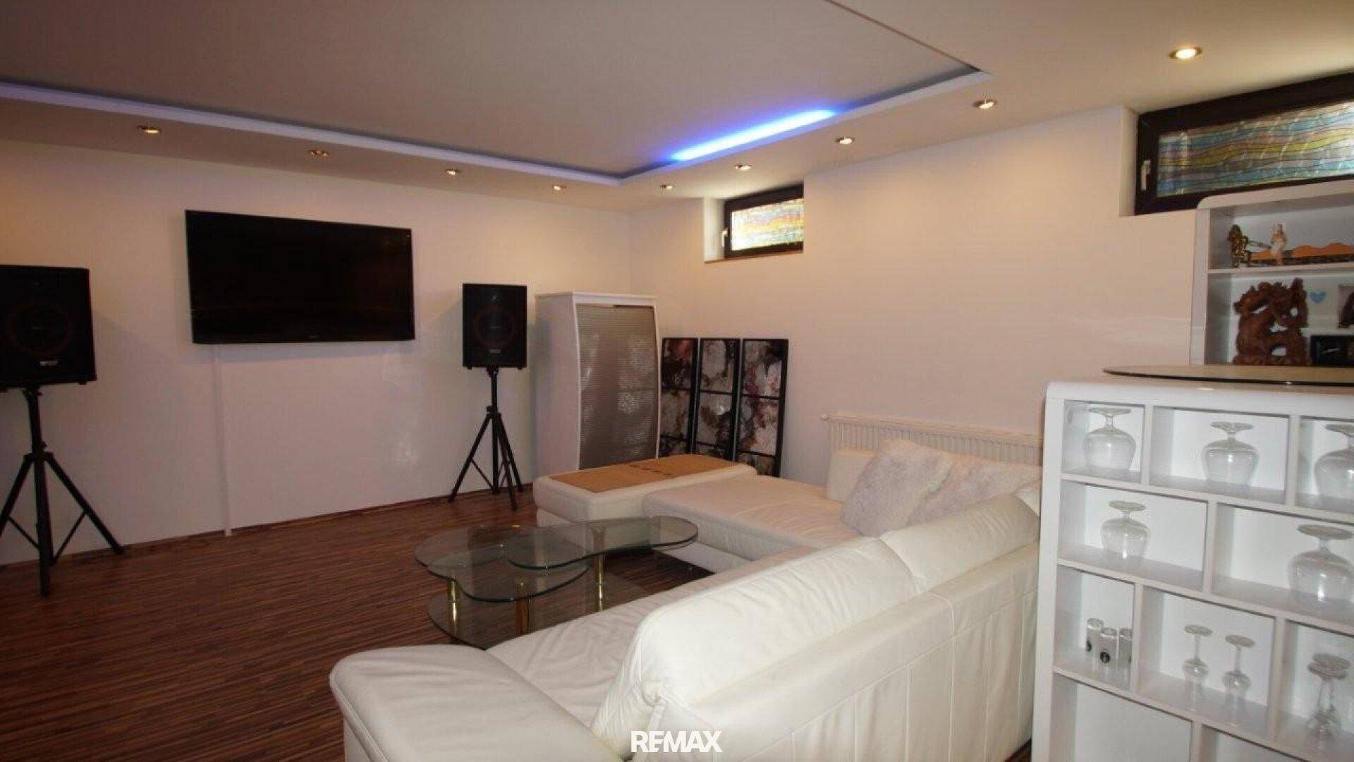 Medienbereich im Keller mit großem Fernseher, Soundsystem und weißem Sofa.