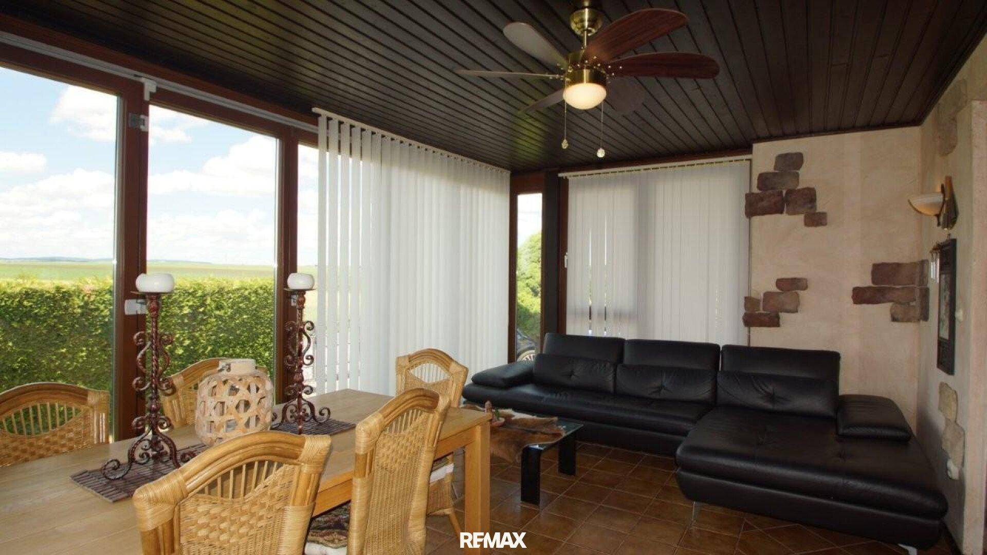 Heller Wintergarten mit Sitzbereich, Deckenventilator und weitem Blick in die Landschaft.