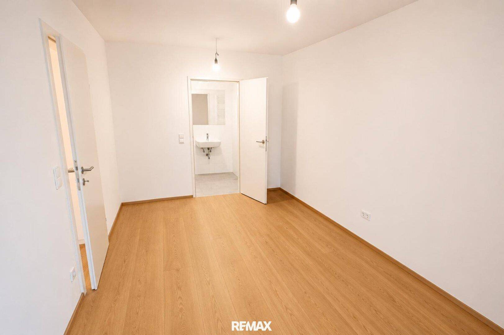 Leeres Schlafzimmer mit hellem Laminatboden und direktem Zugang zu einem Badezimmer.