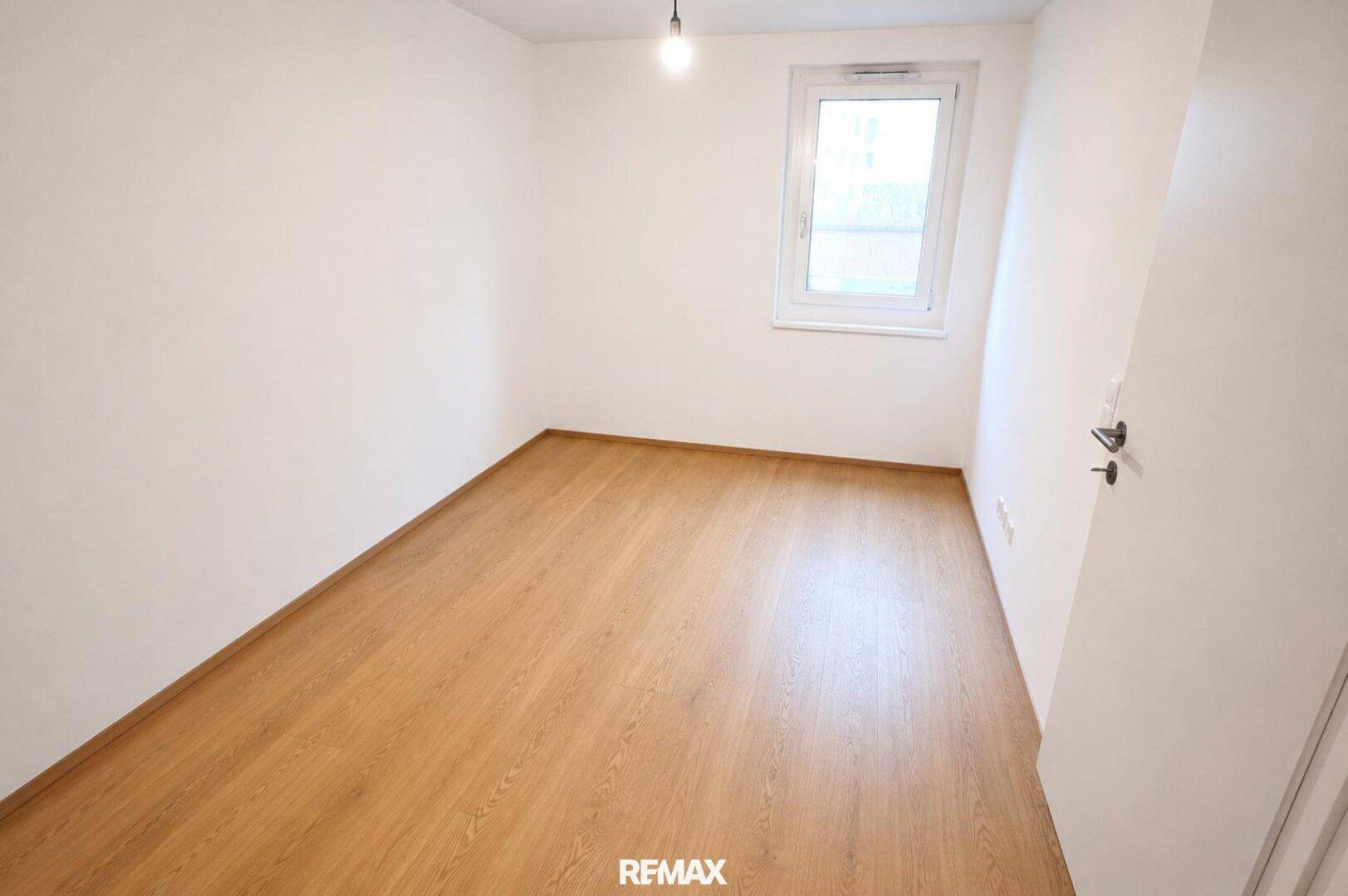 Helles, unmöbliertes Zimmer mit Laminatboden und einem Fenster für Tageslicht.
