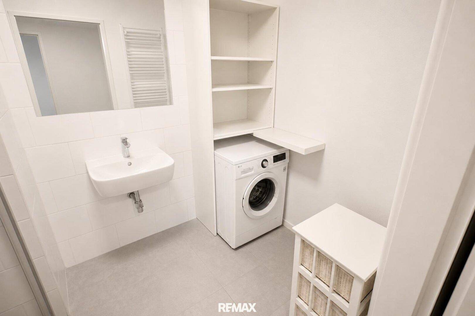 Modernes Badezimmer mit Waschbecken, Spiegel, Handtuchheizkörper und integrierter Waschmaschine.