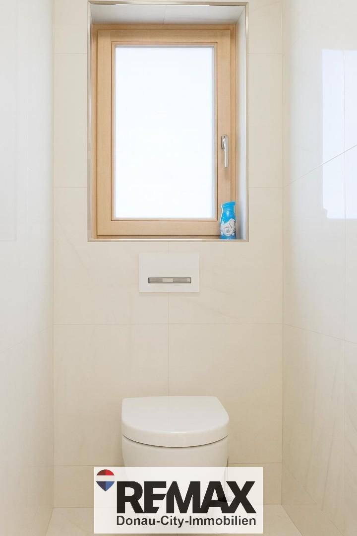 Separates WC mit wandhängender Toilette, Fenster und hellen Fliesen.