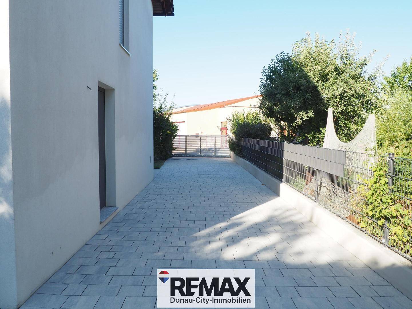 Gepflasterter Weg entlang der Hausseite mit Zaun und Grünflächen.