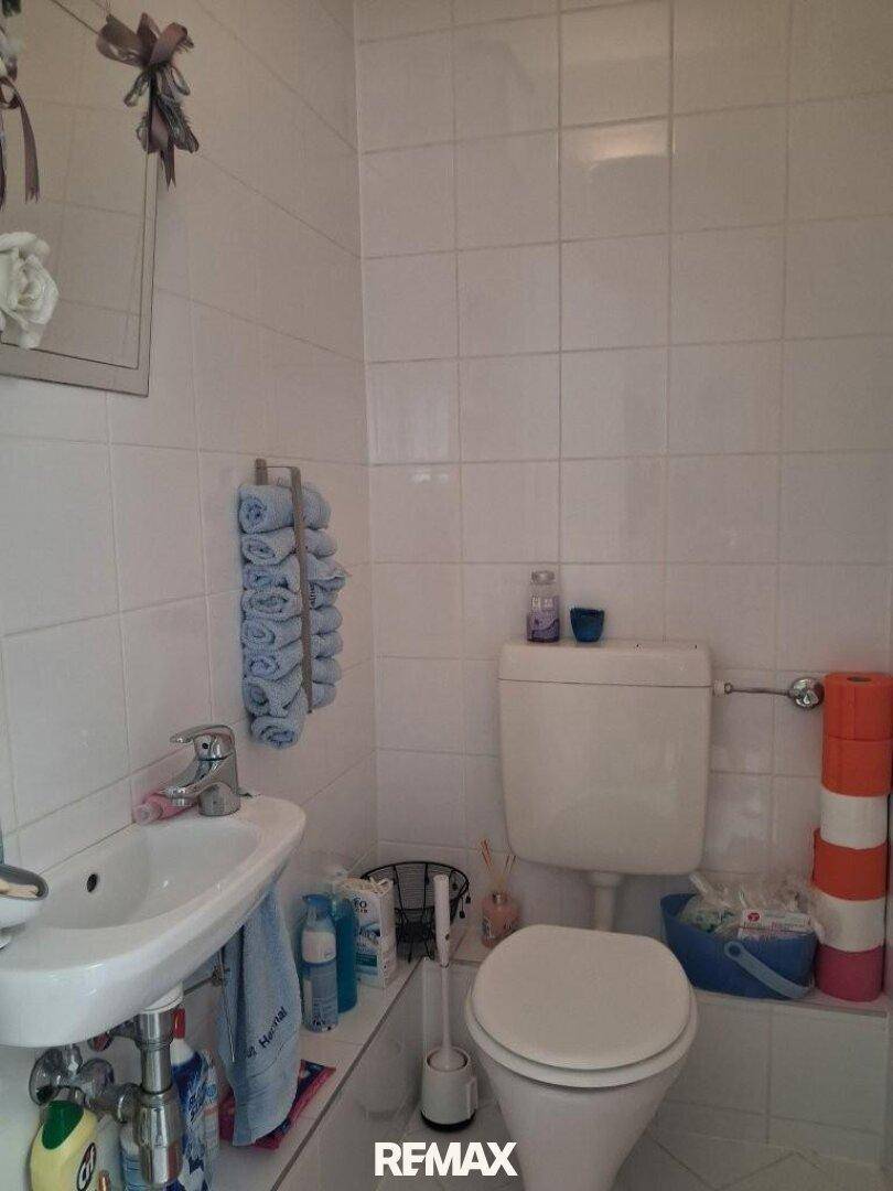 Kleines Gäste-WC mit weißen Fliesen, Waschbecken und Toilette, ohne Fenster.