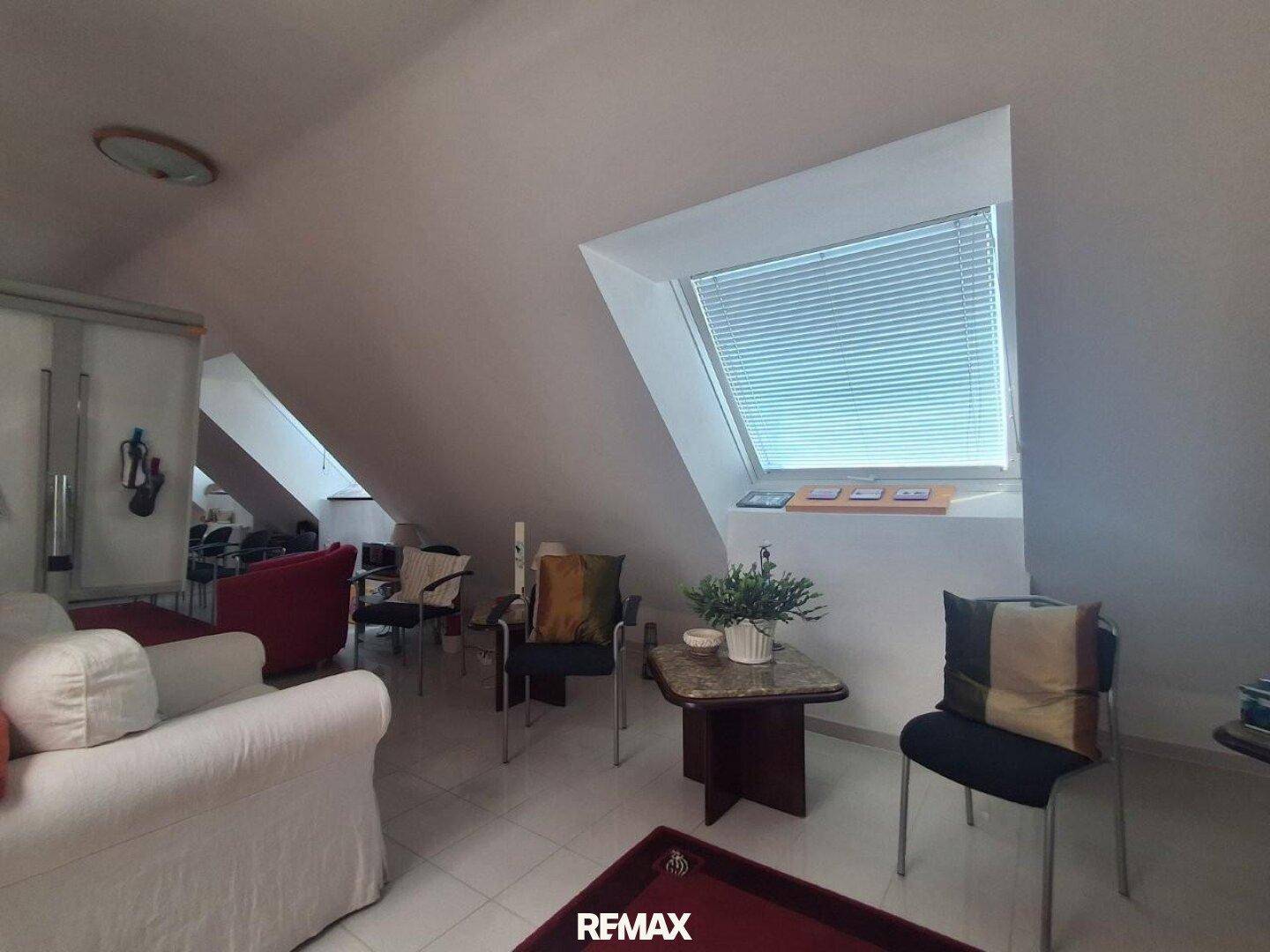 Gemütlicher Wohnbereich im Dachgeschoss mit schrägen Decken, Sofa, Stühlen und einem Dachfenster.