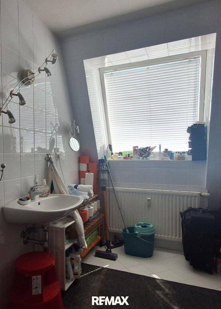 Helles Badezimmer mit weißen Fliesen, Waschbecken und einem großen schrägen Dachfenster.
