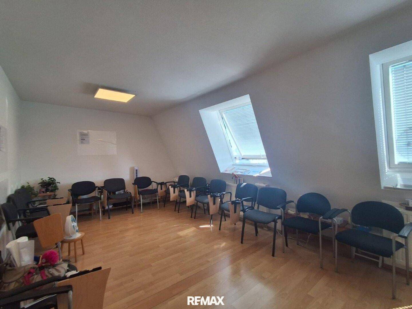 Geräumiger Raum im Dachgeschoss mit Holzfußboden, schrägen Decken und mehreren Bürostühlen.