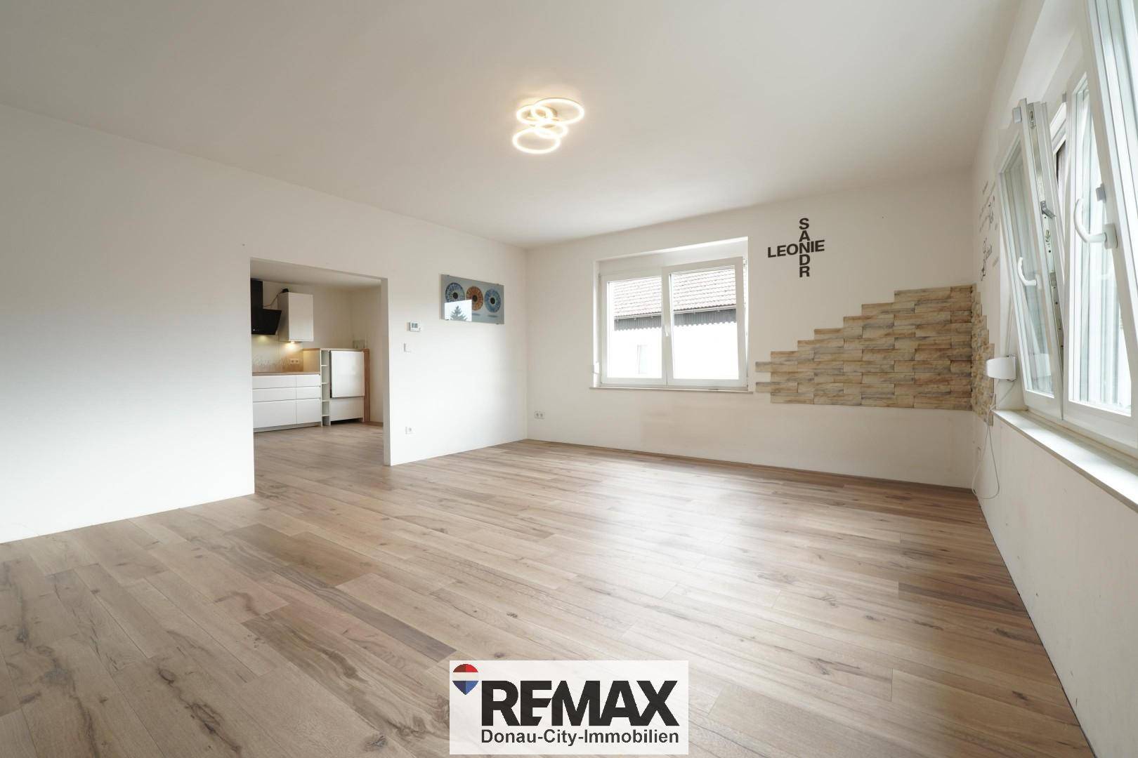 Geräumiges Wohnzimmer mit Holzboden, dekorativer Steinwand und Blick in die angrenzende Küche.