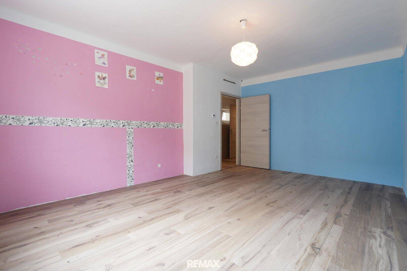 Helles Kinderzimmer mit Holzfußboden und farbenfrohen Akzentwänden in Rosa und Blau.