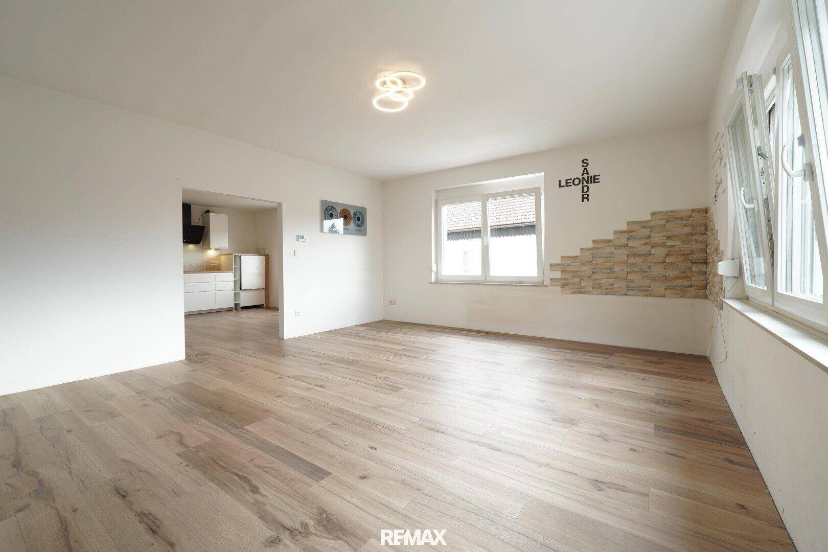 Geräumiges Wohnzimmer mit hellem Holzfußboden, dekorativer Steinwand und Zugang zur Küche.
