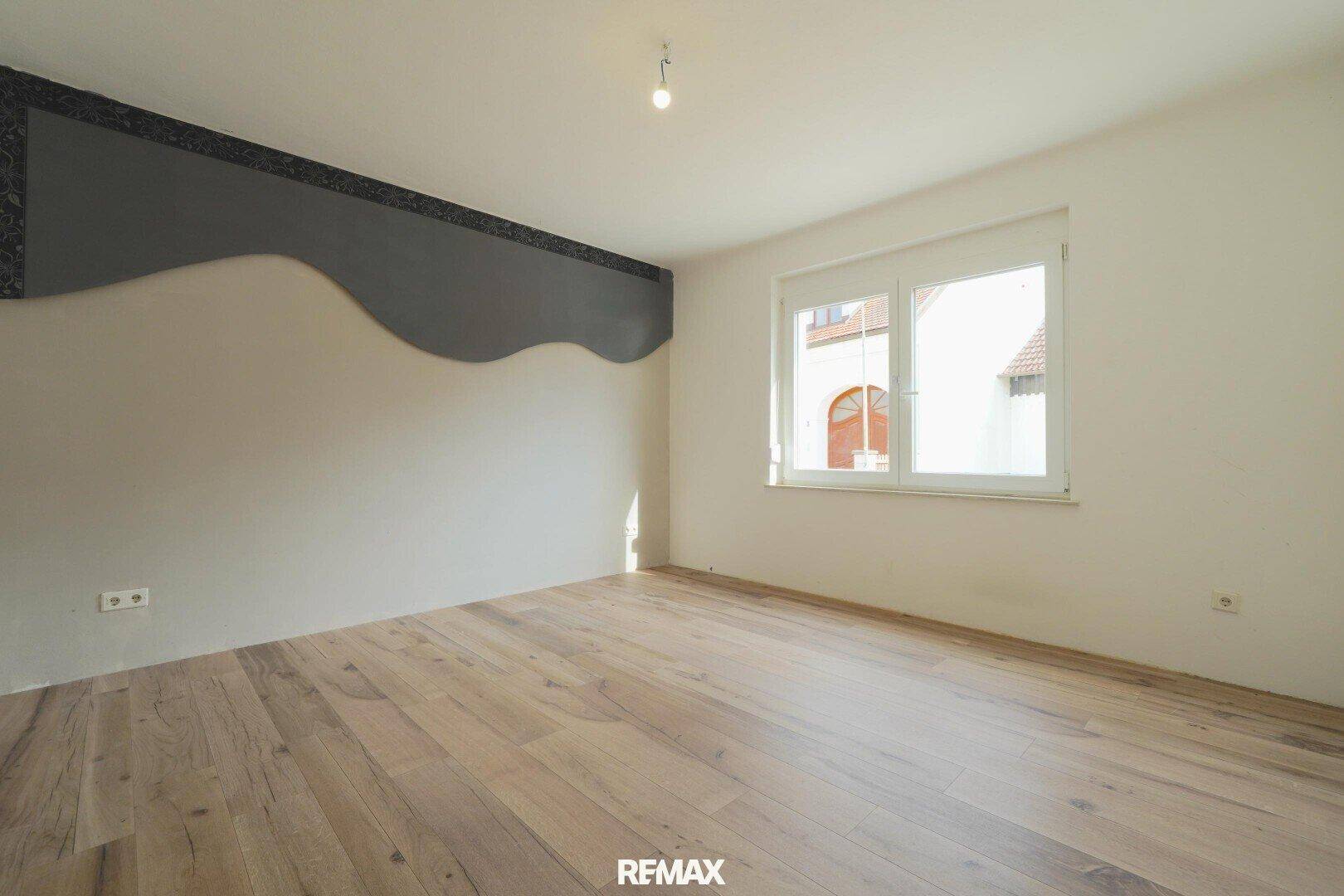 Schlafzimmer mit hellem Holzfußboden, einer dekorativen Wandgestaltung und einem Fenster für natürliches Licht.