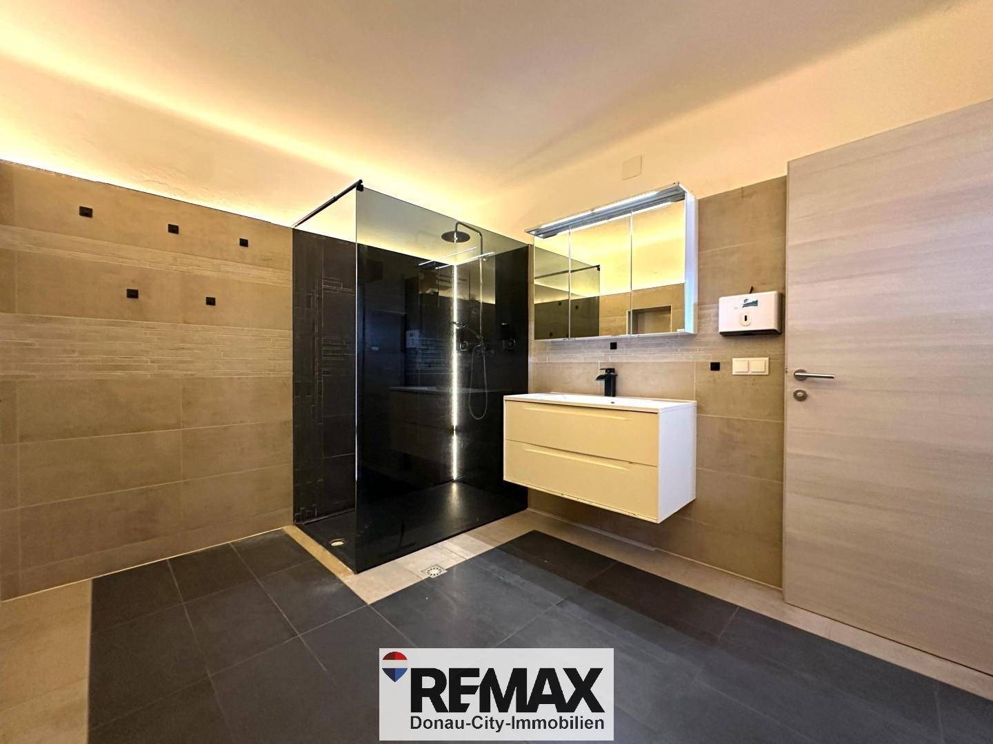 Modernes Badezimmer mit großer begehbarer Dusche, Waschtisch und dunklen Fliesen.
