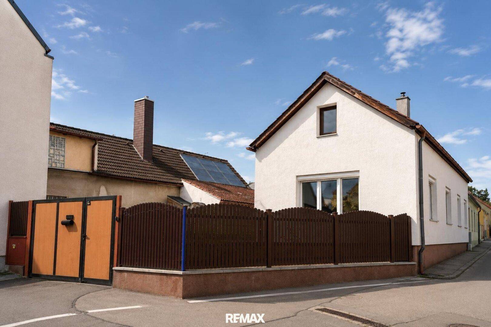 Seitenansicht des Hauses mit braunem Zaun und Photovoltaikanlage auf dem Nachbardach.