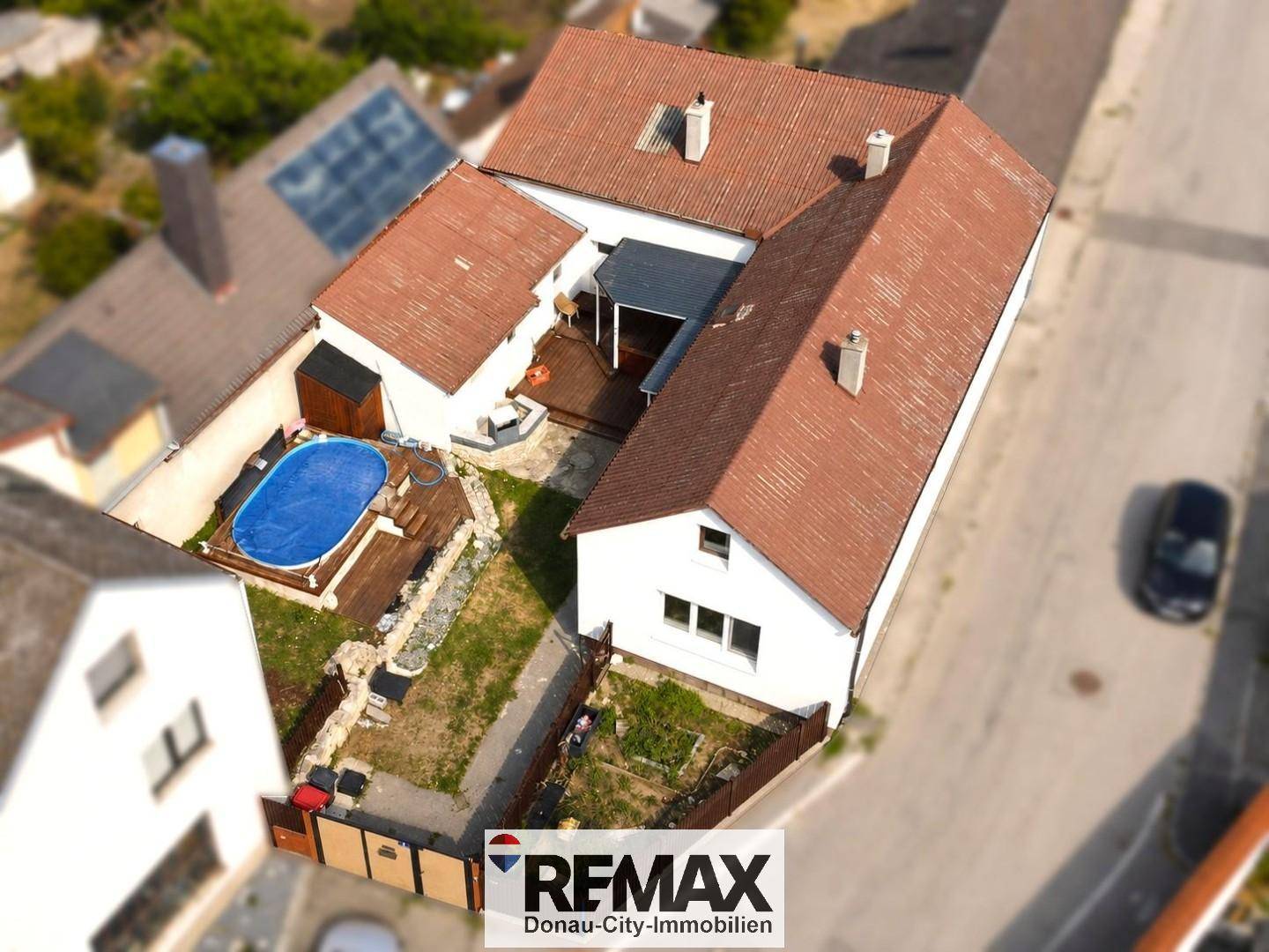 Luftaufnahme des Anwesens mit Haus, Garten, Pool und umliegender Bebauung.