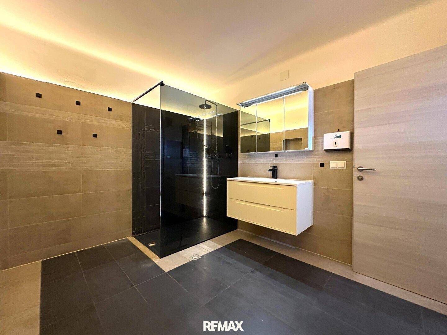 Modernes Badezimmer mit großer begehbarer Dusche, Regenbrause, Einzelwaschbecken und eleganten Fliesen.