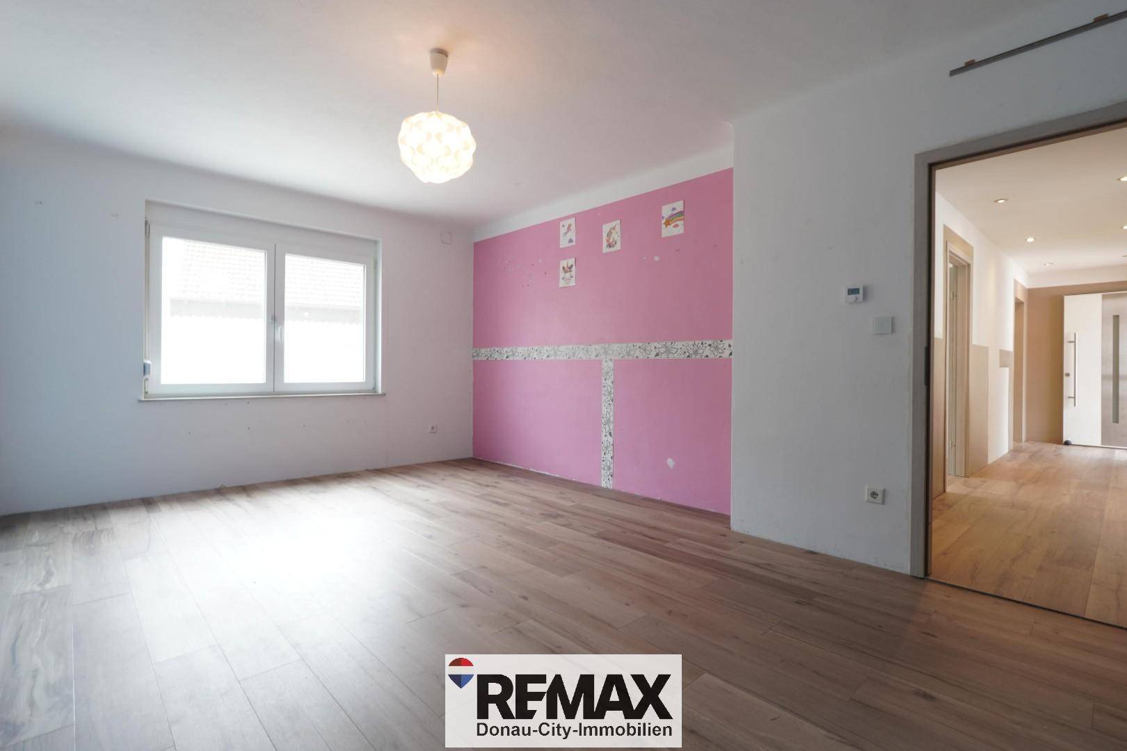 Helles Schlafzimmer mit Holzboden, Fenster und einer auffälligen rosa Akzentwand.