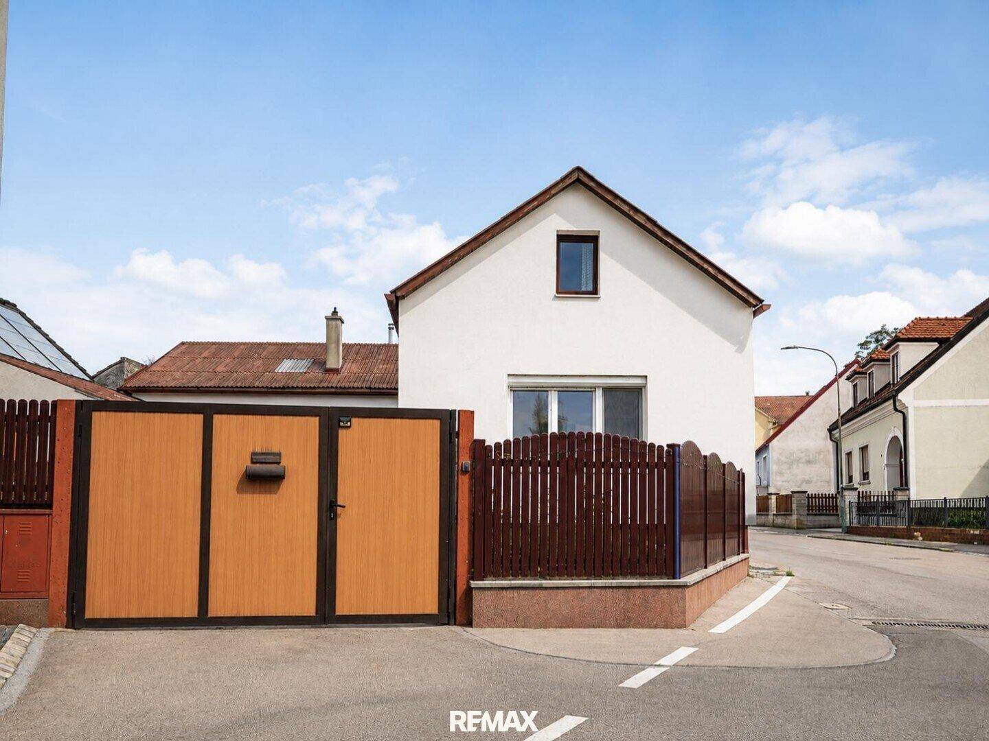 Vorderansicht eines Einfamilienhauses mit braunem Zaun, Tor und Zugang zur Straße.