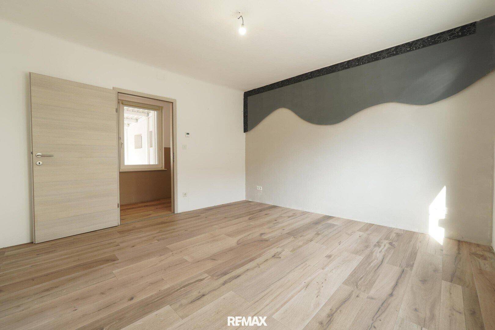 Geräumiges Schlafzimmer mit Holzfußboden, dekorativer Wand und Zugang zu einem weiteren Raum.