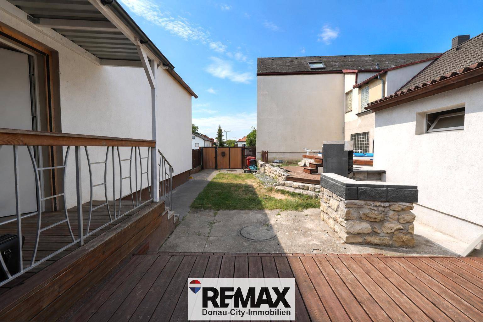 Hinterhof mit Holzterrasse, Rasenfläche und einem Bereich für Outdoor-Aktivitäten.