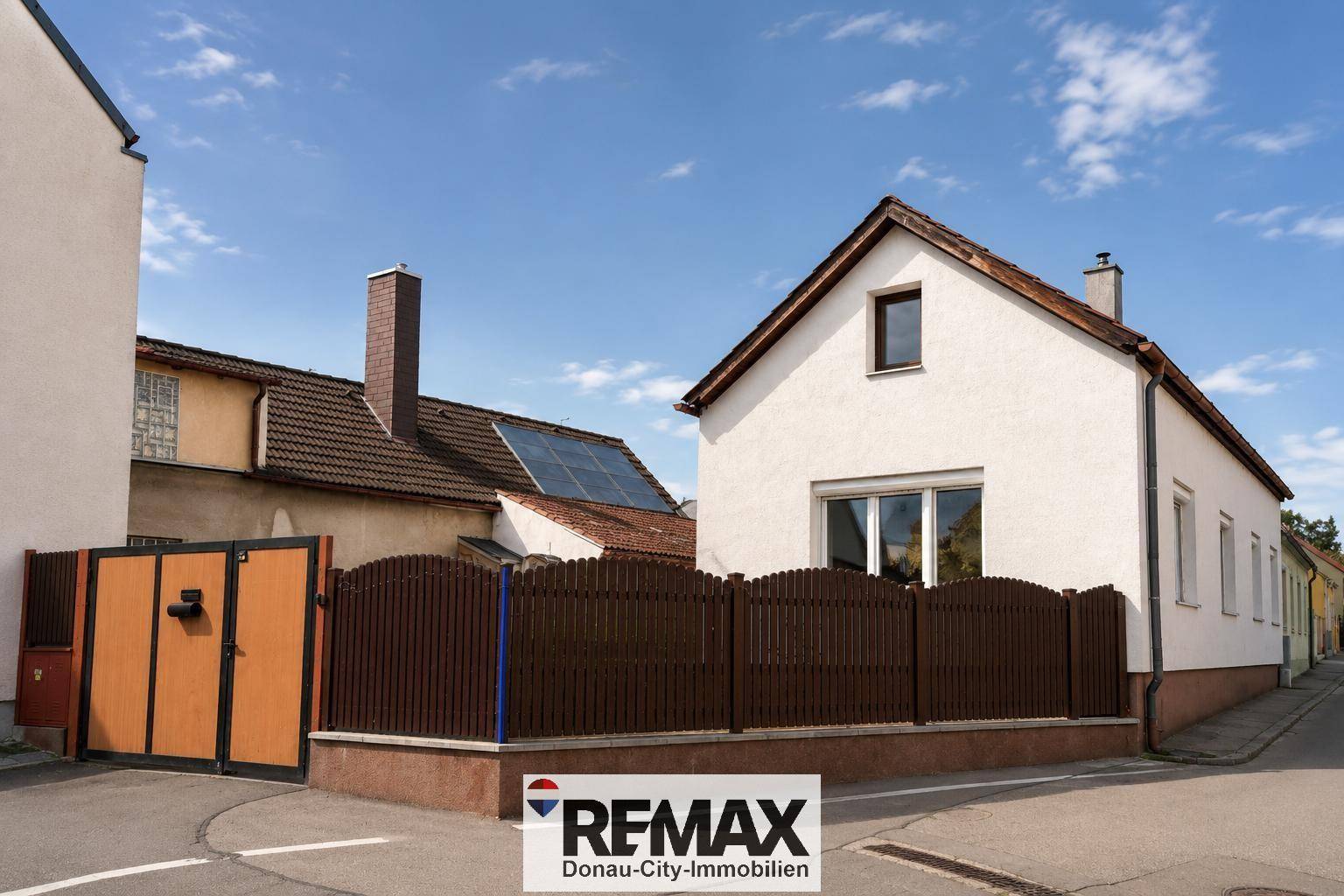 Seitenansicht des Hauses mit Satteldach, Zaun und Solarpaneelen auf dem Dach.