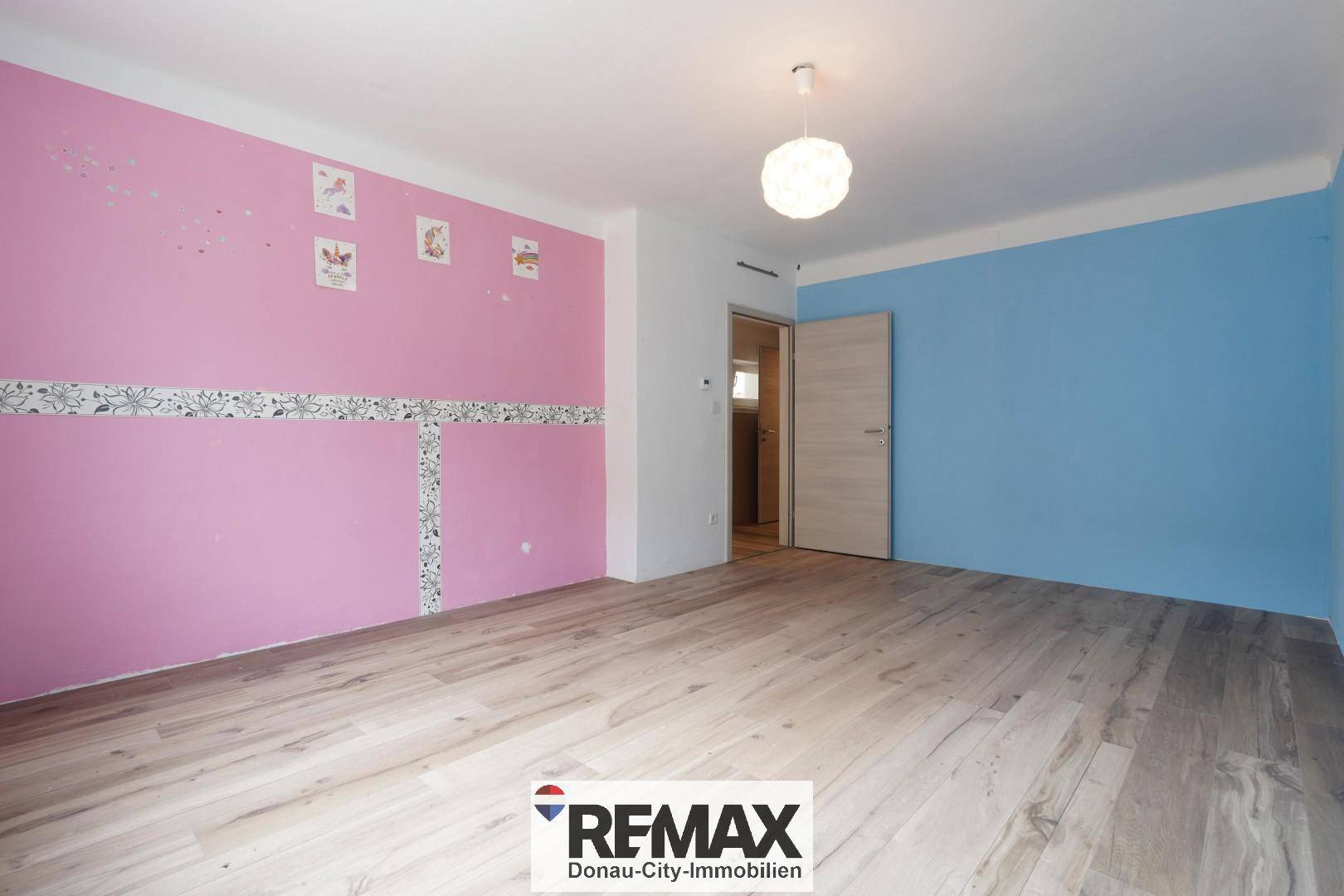 Schlafzimmer mit Holzboden und farbenfrohen Wänden in Rosa und Blau.