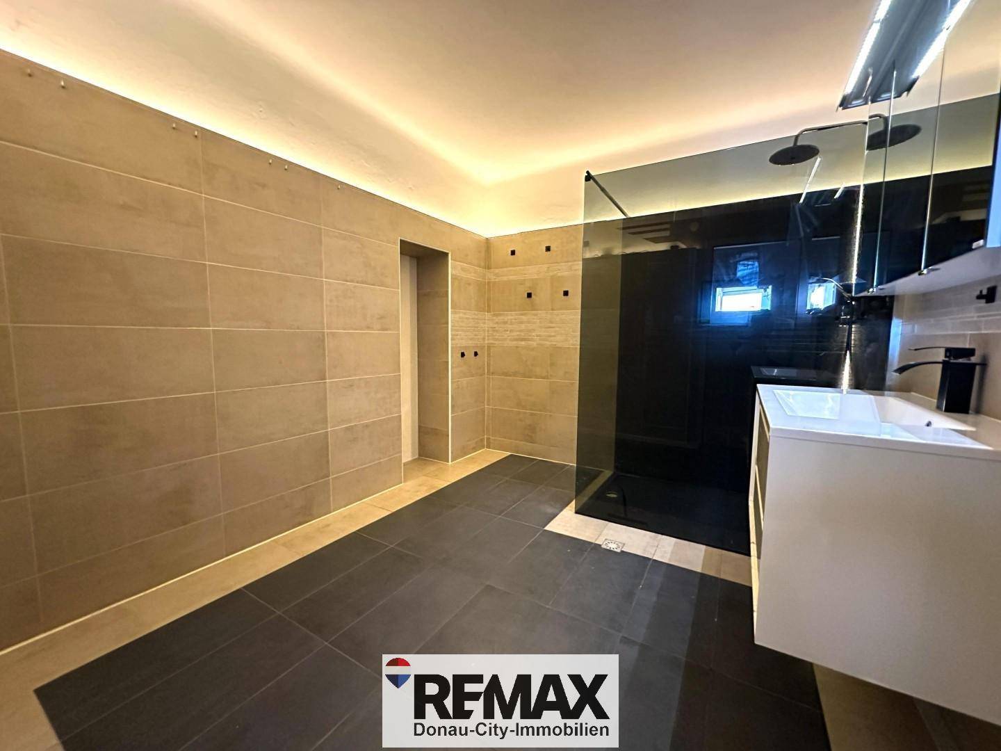 Geräumiges Badezimmer mit begehbarer Dusche und modernen Fliesen an Wänden und Boden.