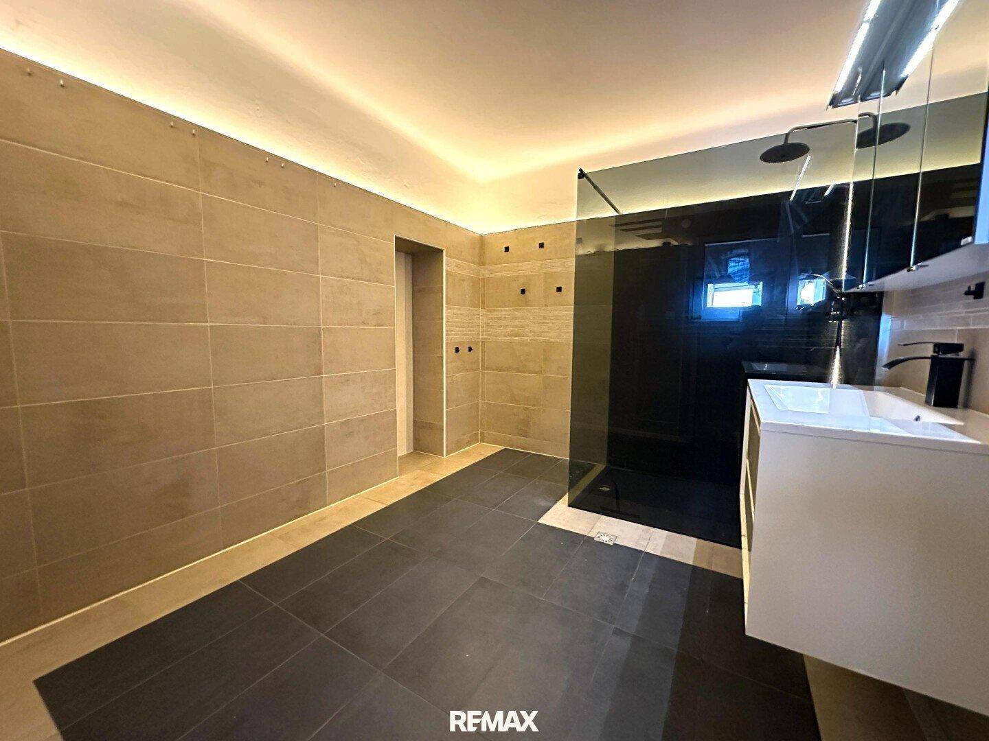 Geräumiges Badezimmer mit modernen Fliesen, begehbarer Dusche und indirekter Beleuchtung.