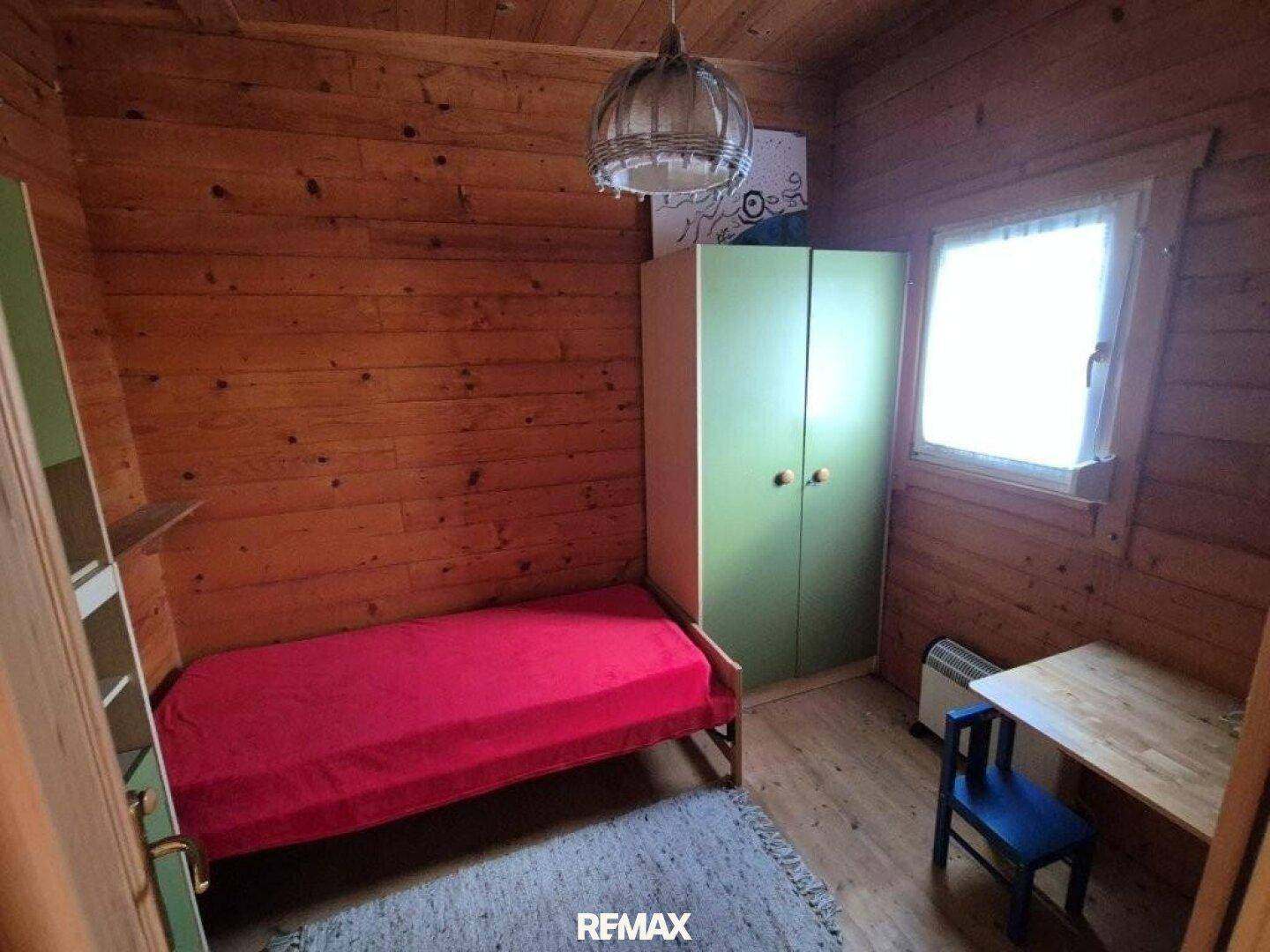 Kleines Schlafzimmer mit Holzvertäfelung, Einzelbett und grünem Kleiderschrank.