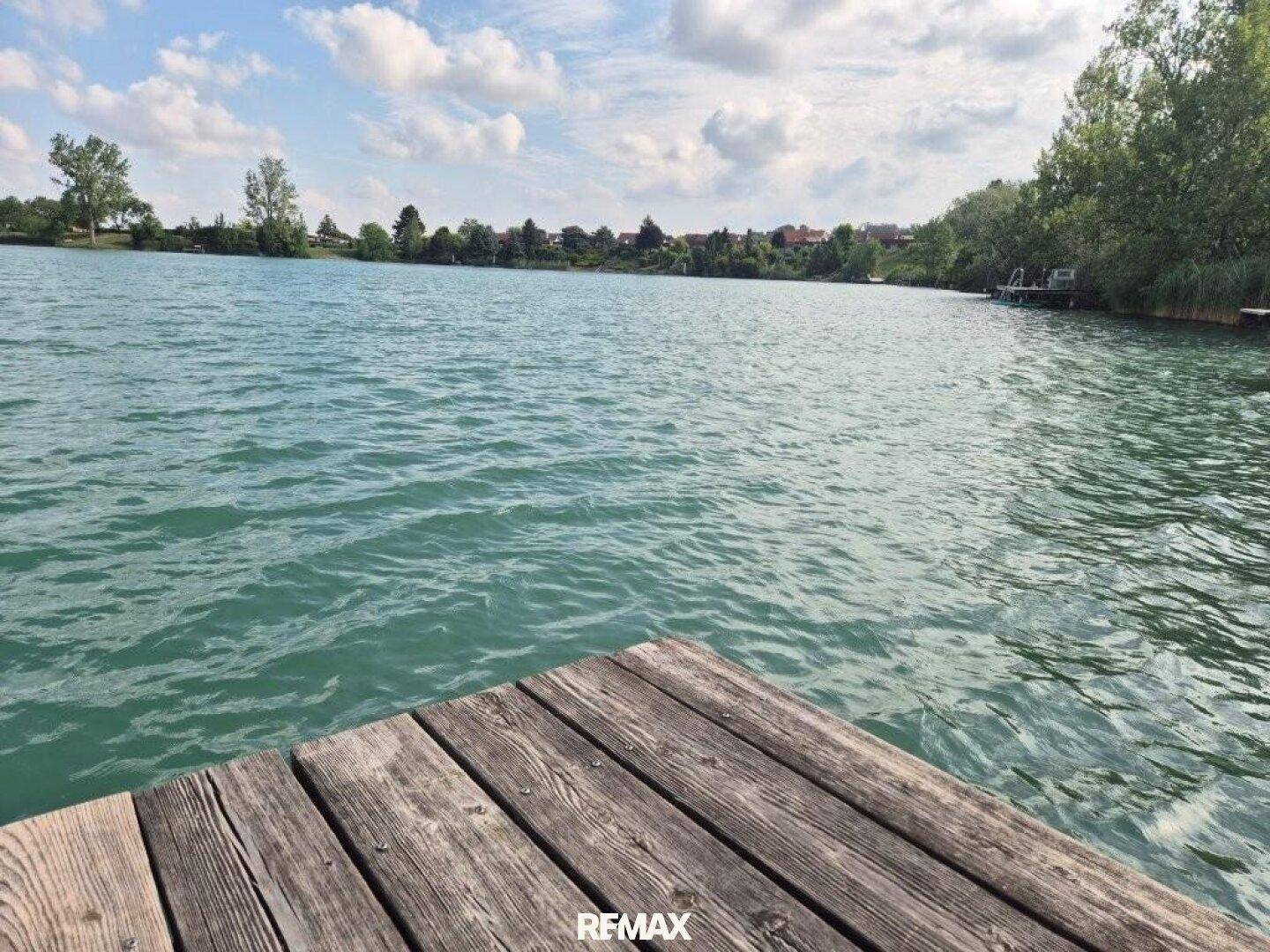 Malerischer Seeblick von einem Holzsteg unter blauem Himmel mit Wolken.