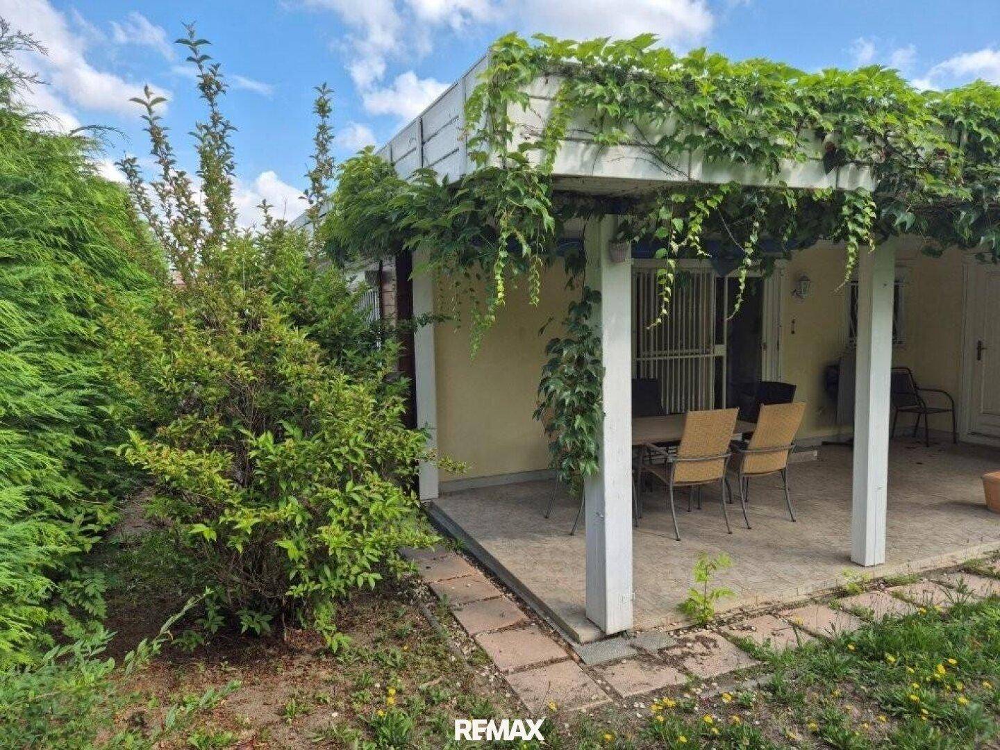 Grüner Gartenbereich mit überdachter Terrasse und üppiger Vegetation.