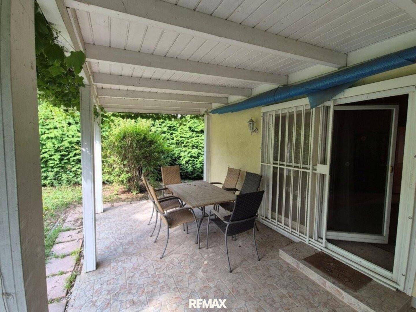 Überdachte Terrasse mit Sitzgelegenheiten und Blick auf die grüne Hecke im Garten.