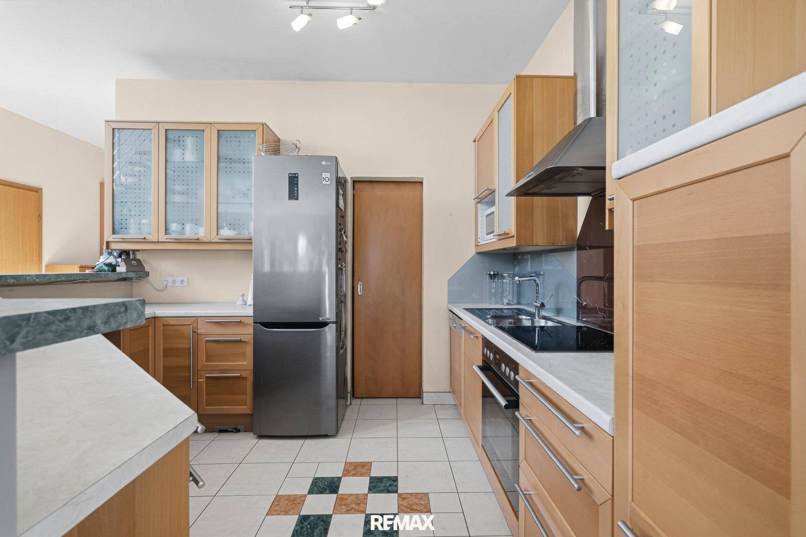 Funktionale Küche mit Holzschränken, Fliesenboden und modernen Geräten.