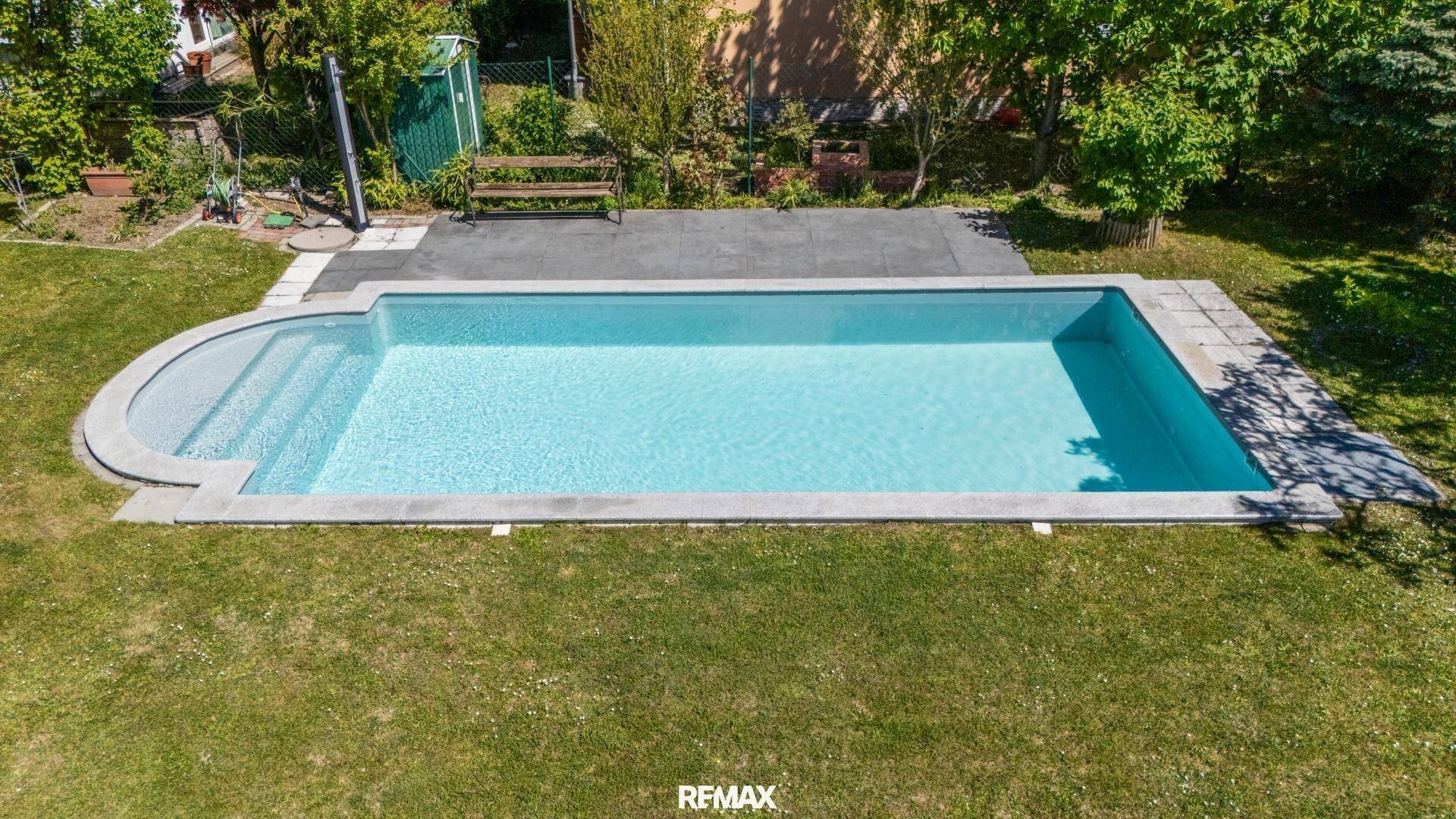 Rechteckiger Swimmingpool im Garten mit gepflastertem Bereich und Rasen.