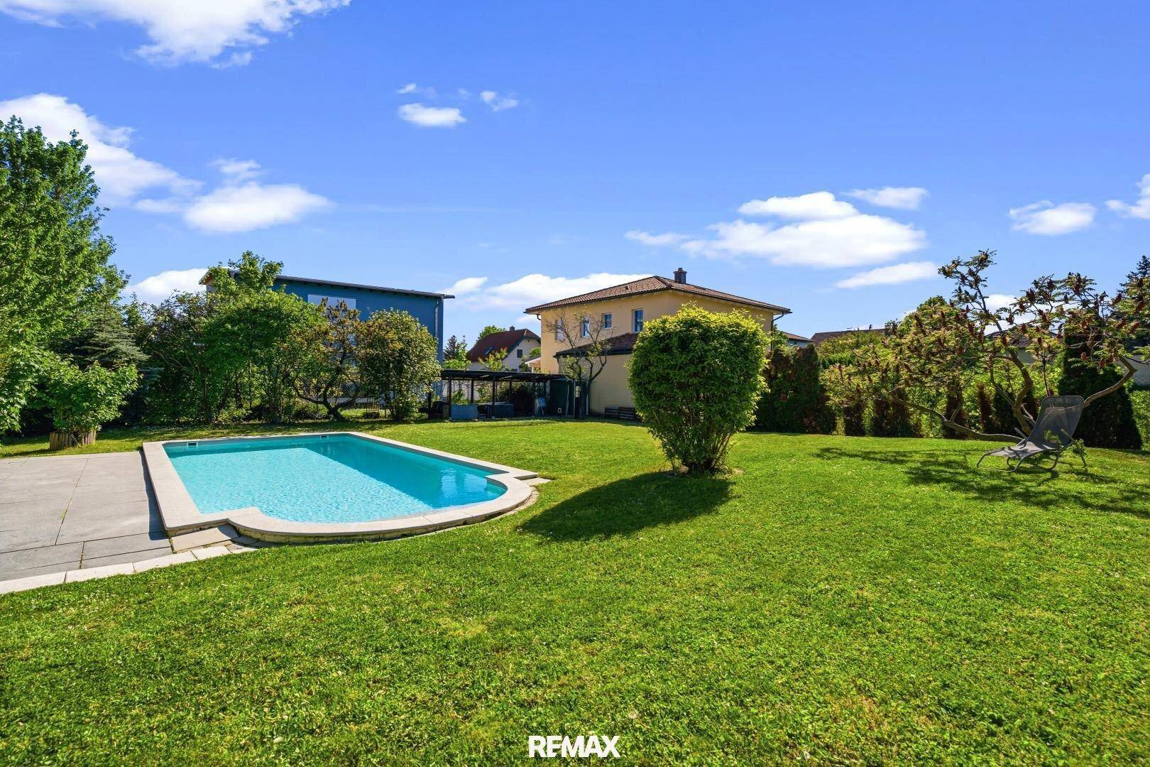 Weitläufiger Garten mit Swimmingpool und viel Grünfläche unter blauem Himmel.