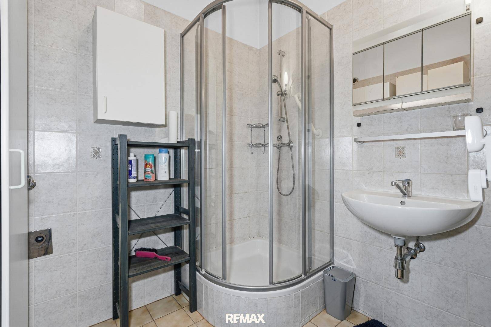 Kleines Badezimmer mit Duschkabine, Waschbecken und Spiegelschrank.