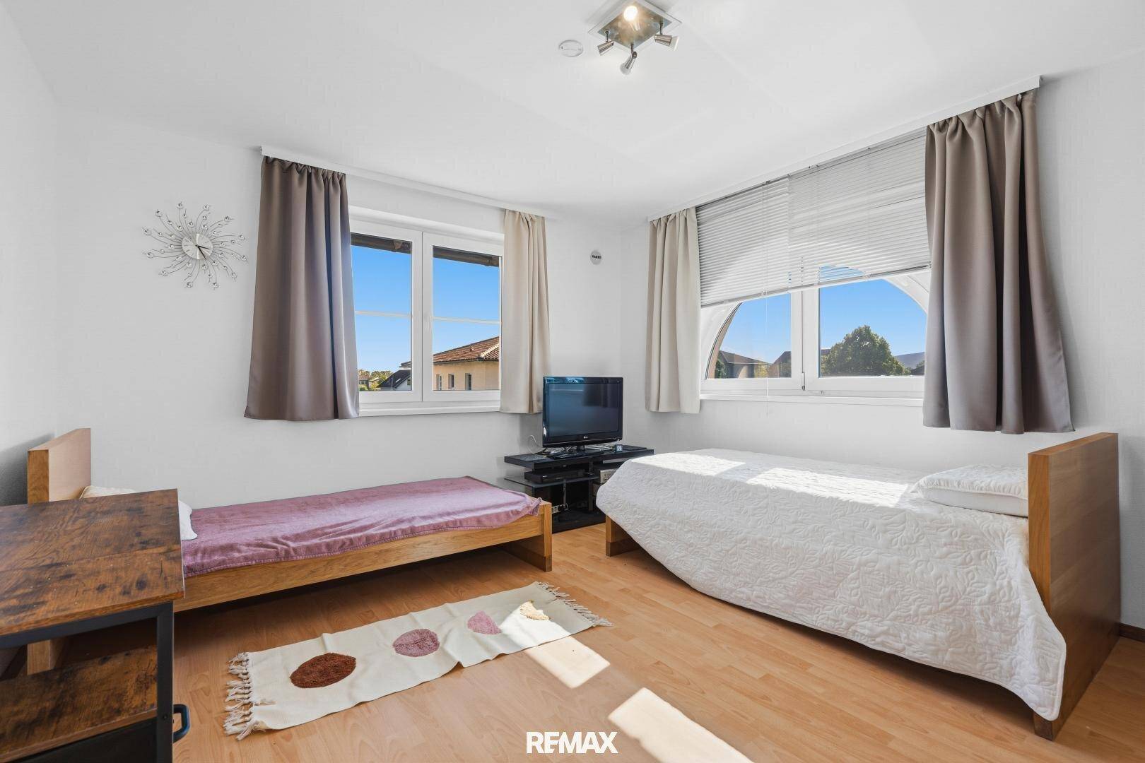 Helles Schlafzimmer mit zwei Einzelbetten, Holzboden und großen Fenstern.